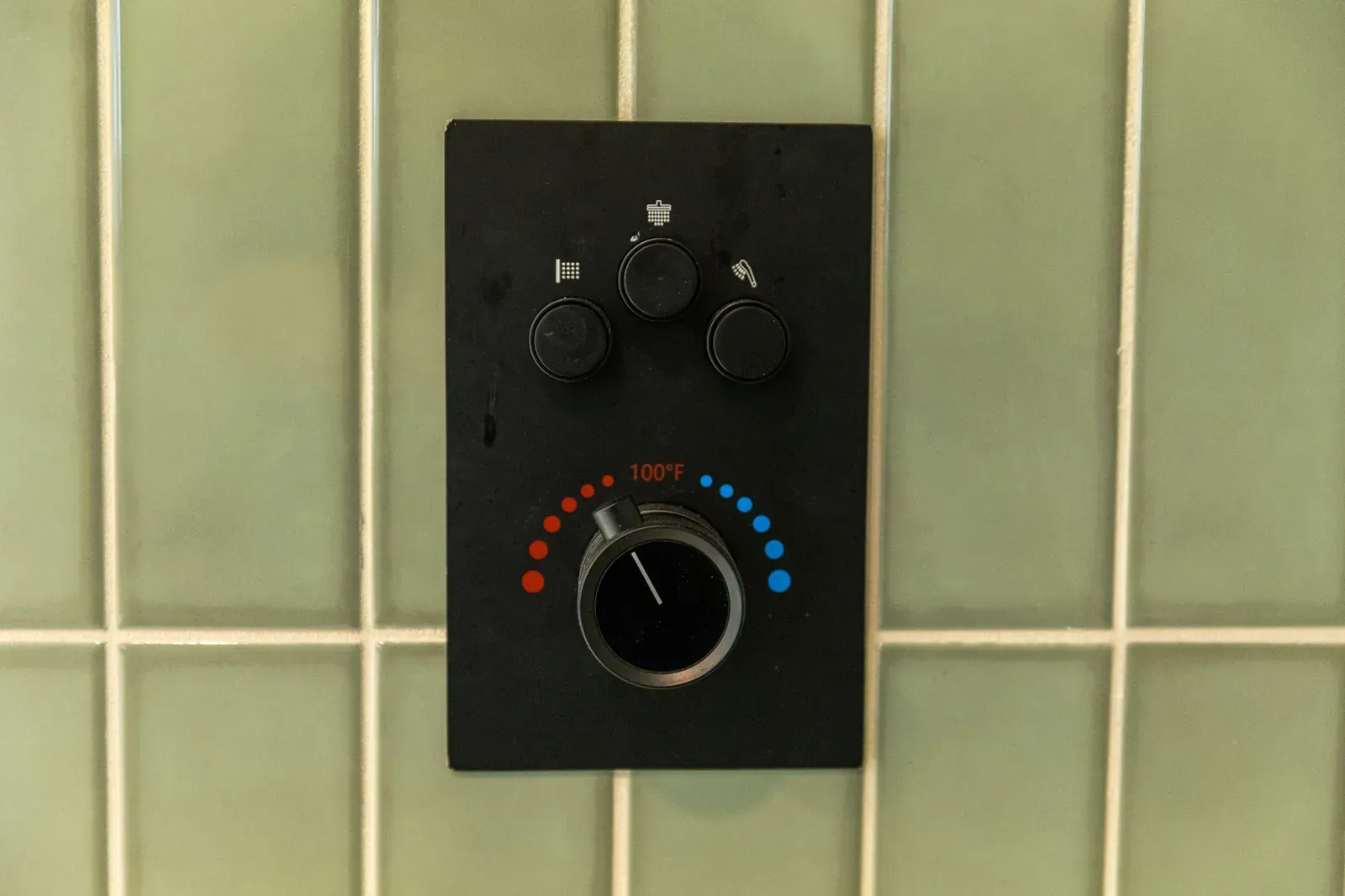 Black shower control panel with three knobs on green tiled wall