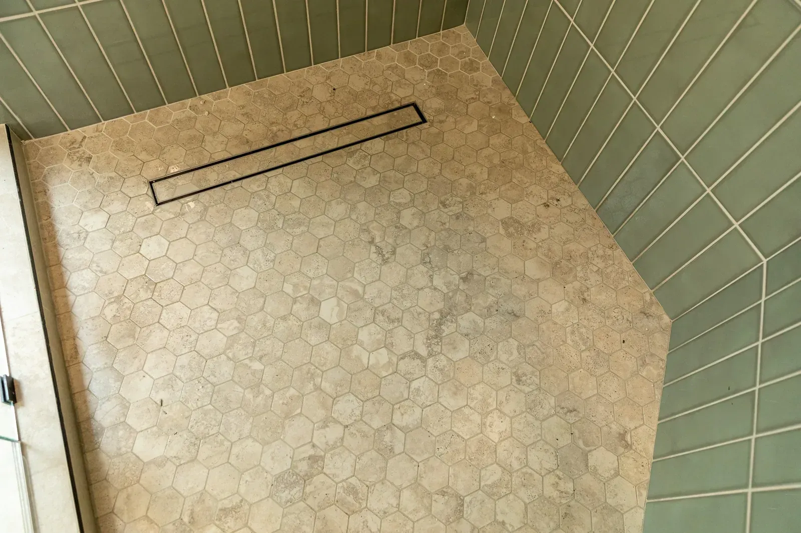 Empty green-tiled shower stall with hexagonal floor tile and a metal drain