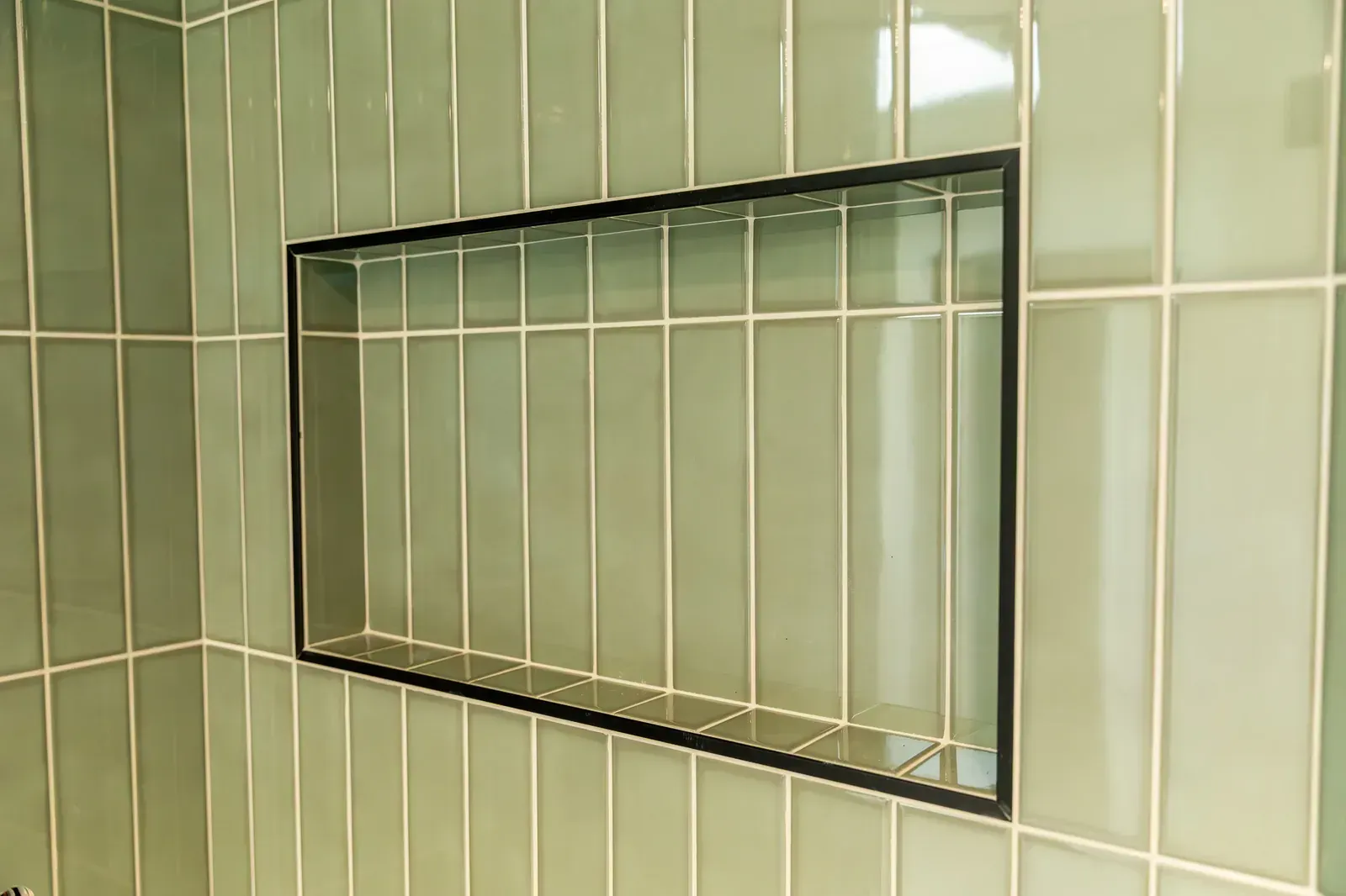 Rectangular wall mirror framed in black, set against pale green tiled bathroom walls.