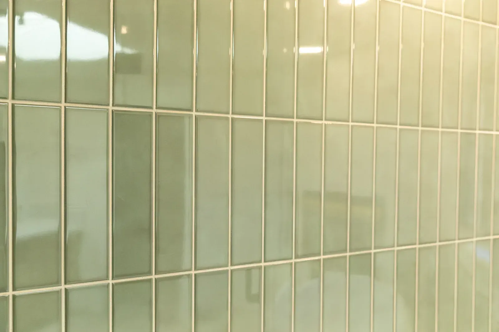 Close-up of pale green tiled wall with reflections and vertical grout lines