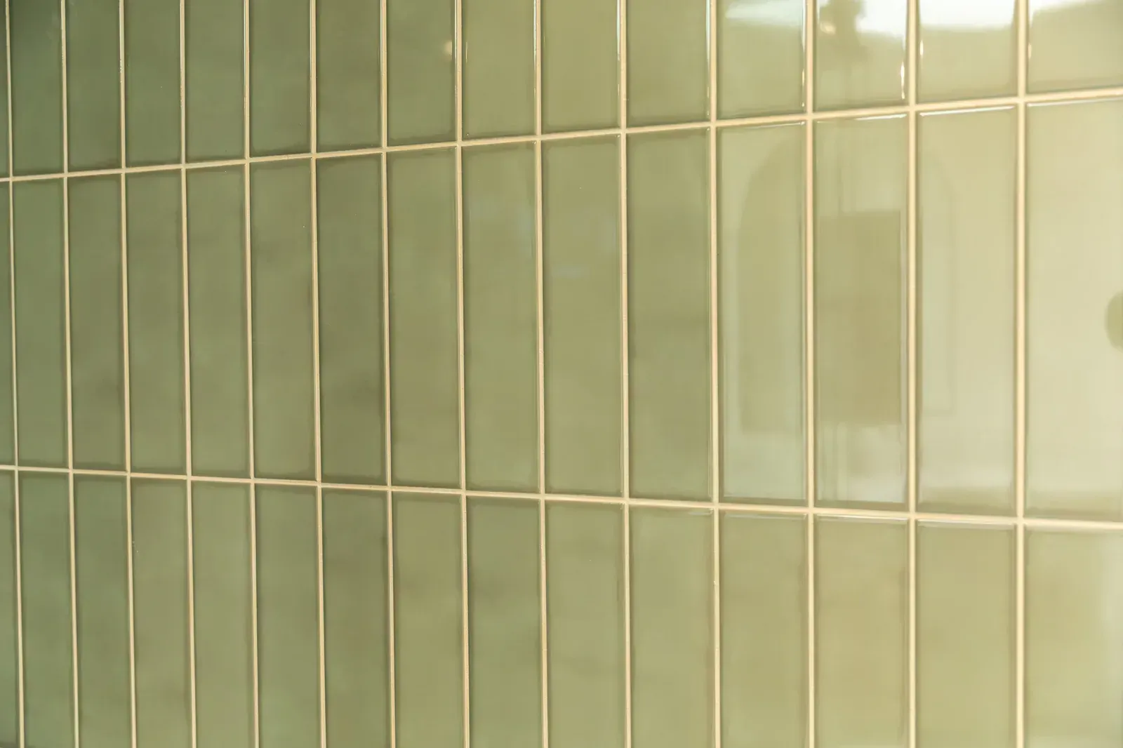 Close-up of pale green ceramic wall tiles with grout lines and reflections