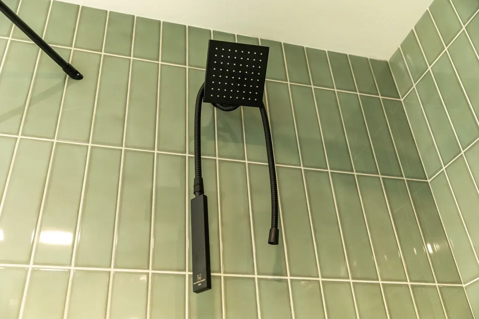 Black shower chair mounted on a pale green tiled bathroom wall with grab bars nearby