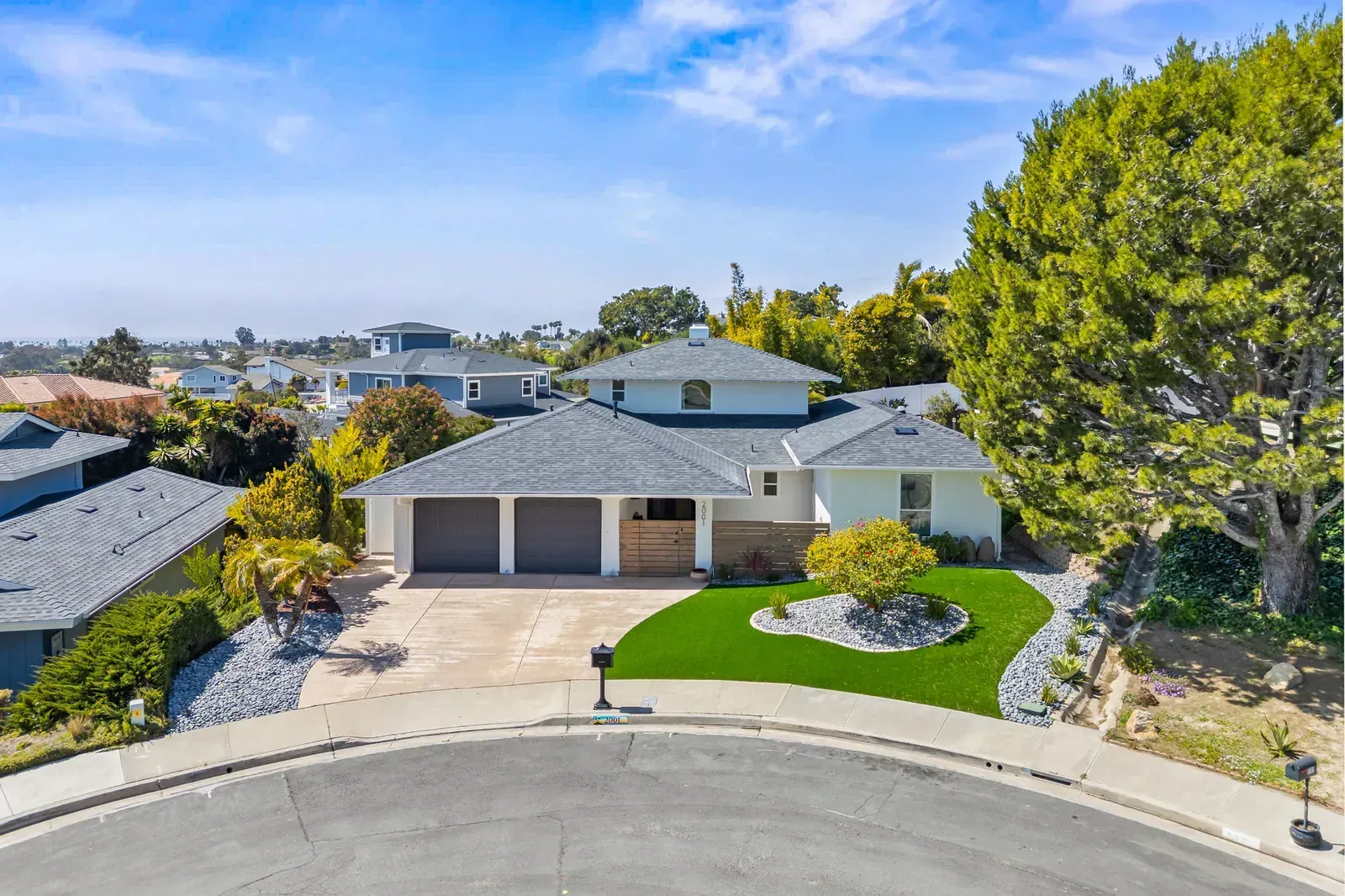 Aerial view of a suburban house with a three-car garage, landscaped front yard, and cul-de-sac street