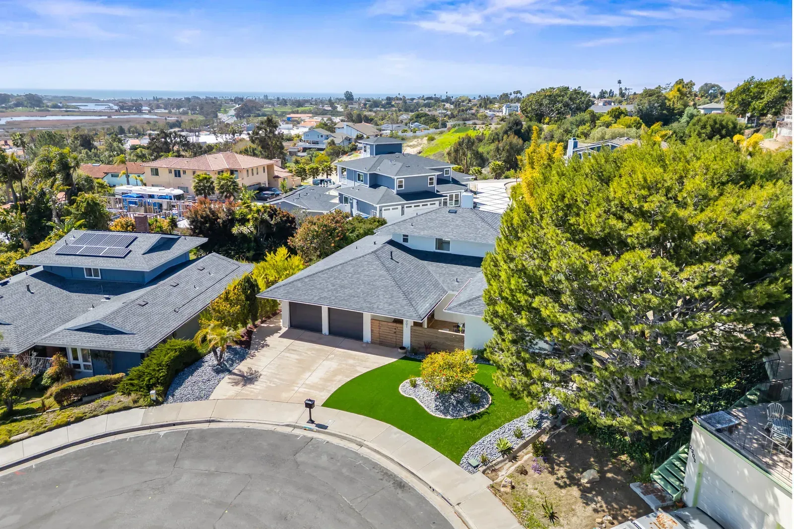 Aerial view of suburban homes on a curved street with trees and a distant city skyline.