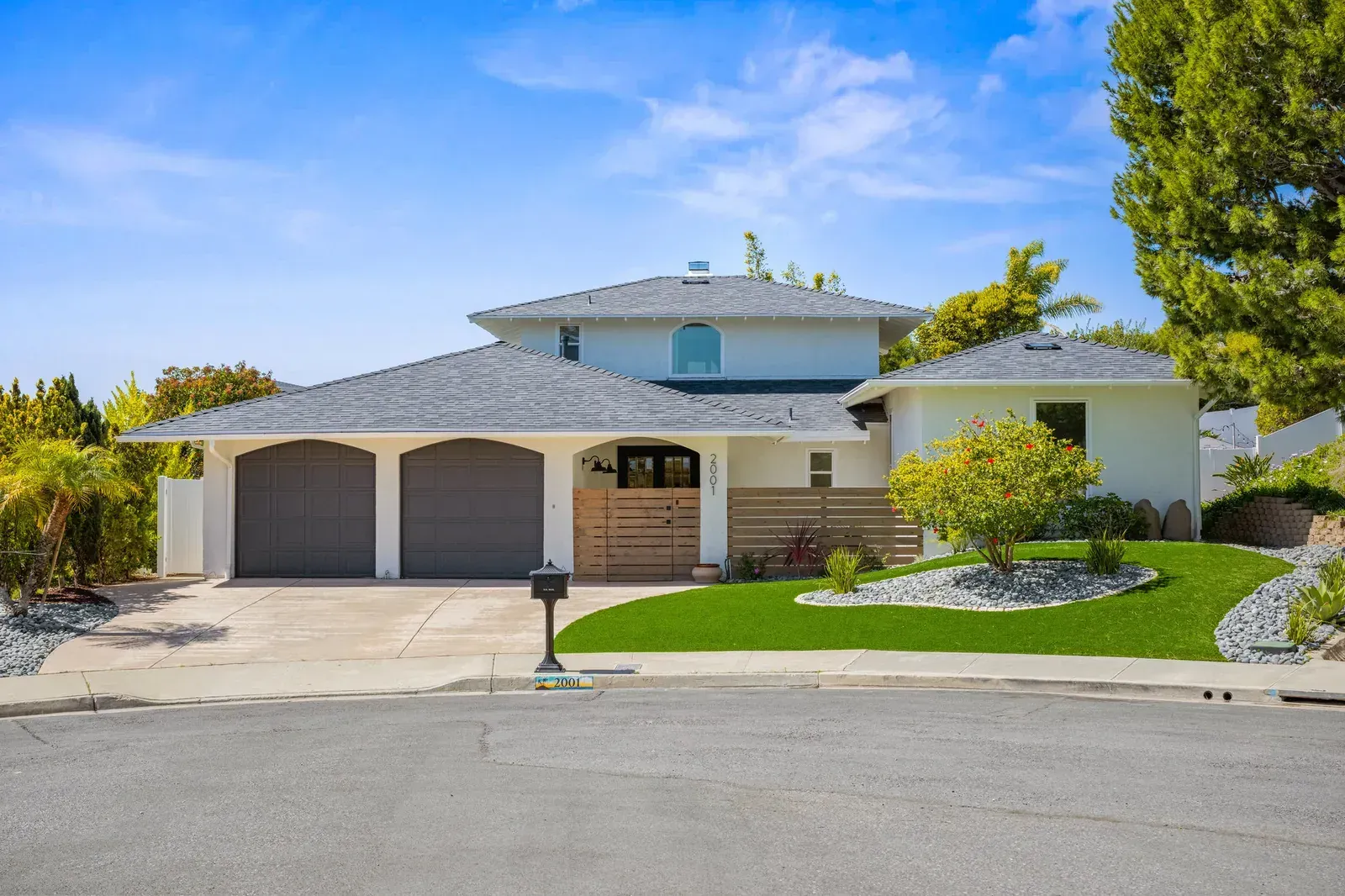 Modern beige house with two garages, landscaped front yard, and blue sky