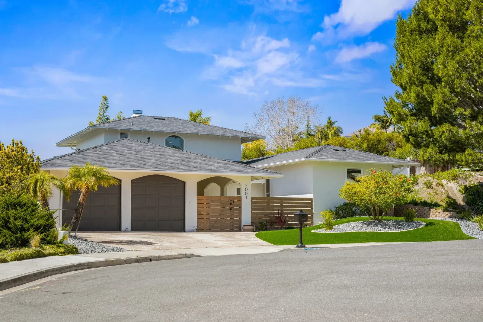 Modern house with a garage, white walls, and a landscaped front yard under a blue sky