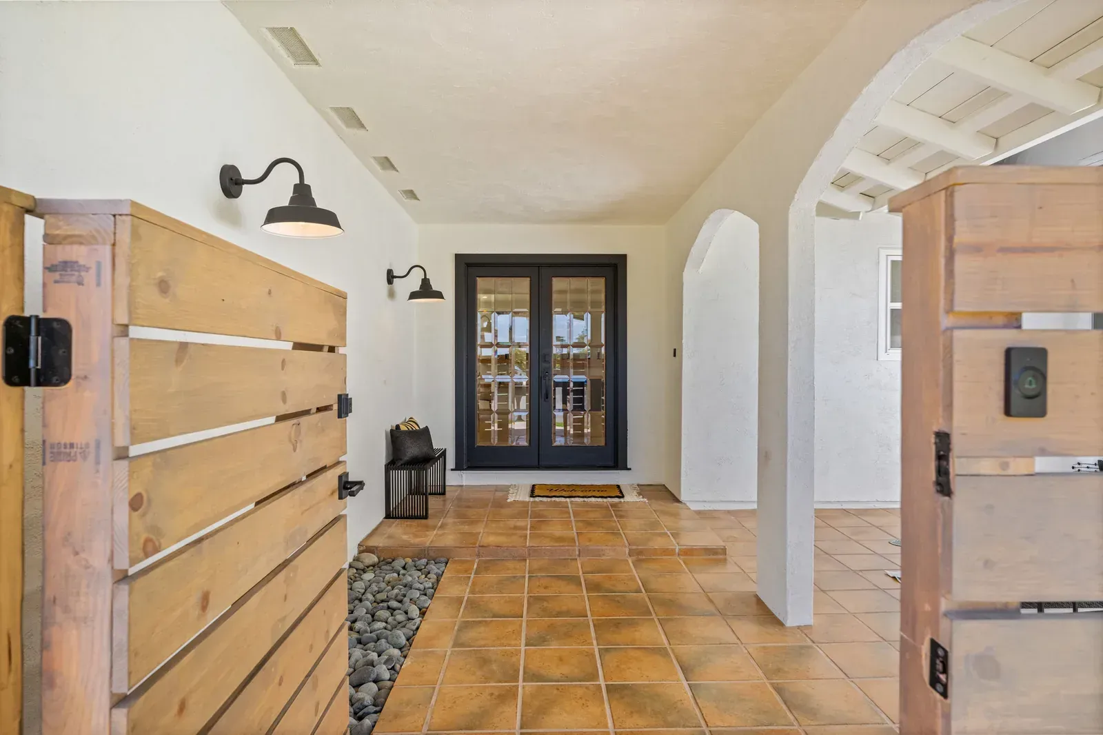 Rustic hallway with terracotta tile, white walls, wooden shutters, and glass doors at the end