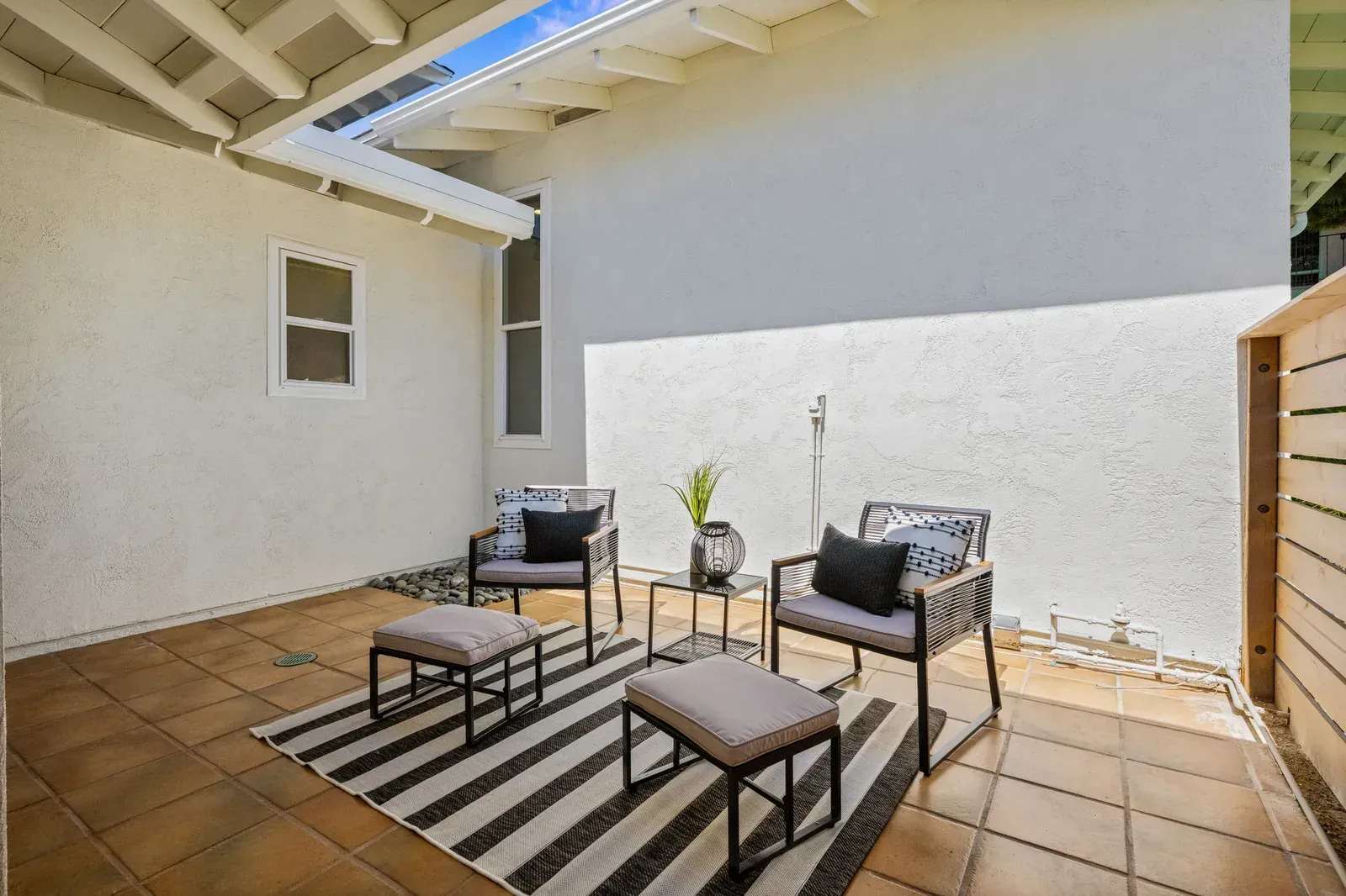 Patio seating area with two armchairs, two side tables, and a striped rug under a shaded overhang
