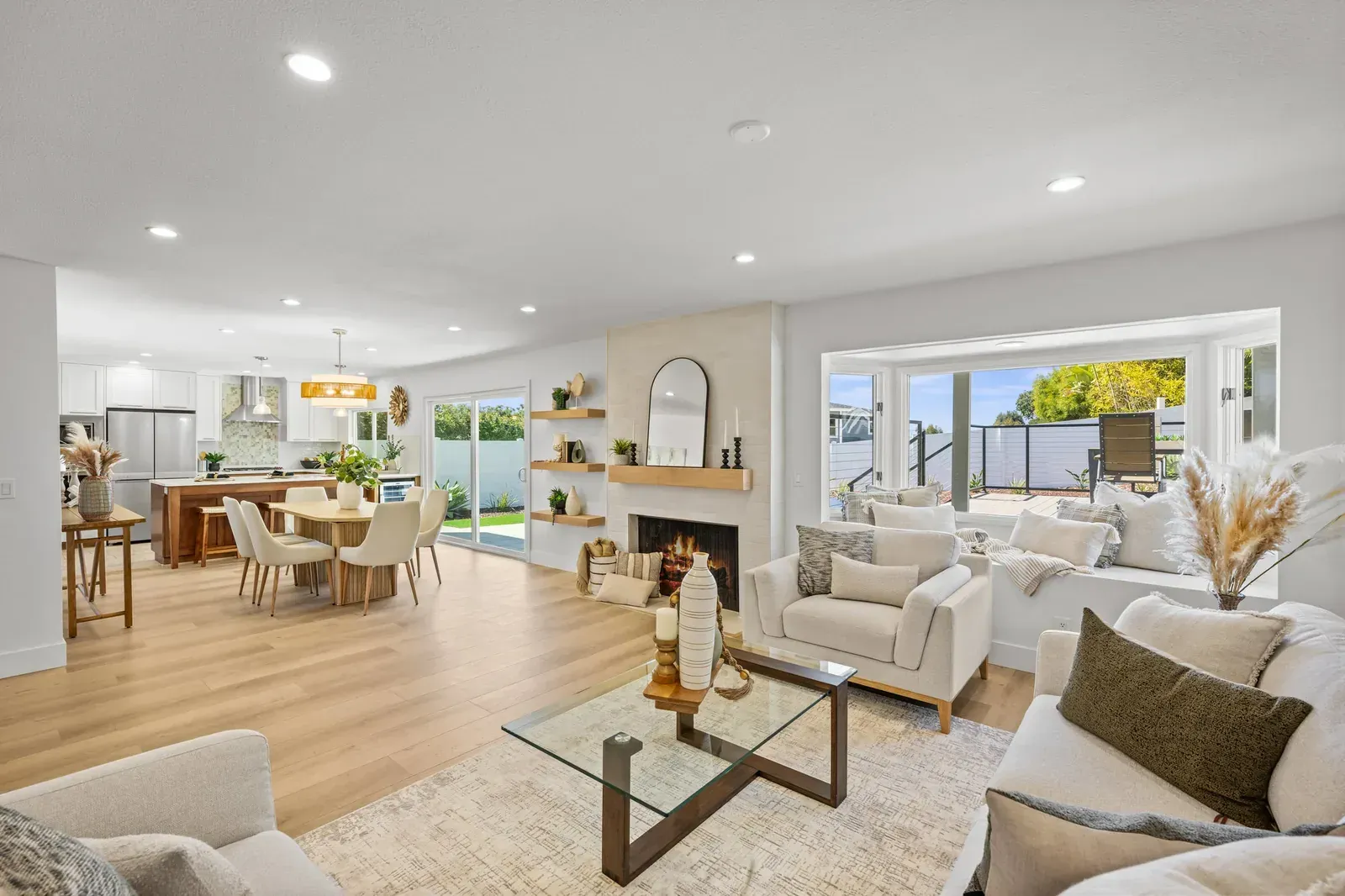 Bright open-plan living room and kitchen with light wood floors, white furniture, and large windows in an Oceanside remodel.