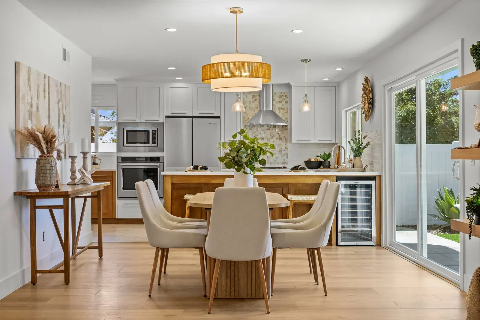Bright modern kitchen and dining area with white cabinets, wood floors, and a sliding glass door to a patio.