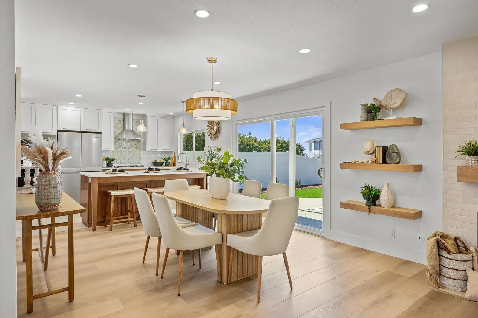 Bright modern dining room with wooden table, beige chairs, gold pendant light, and open garden view