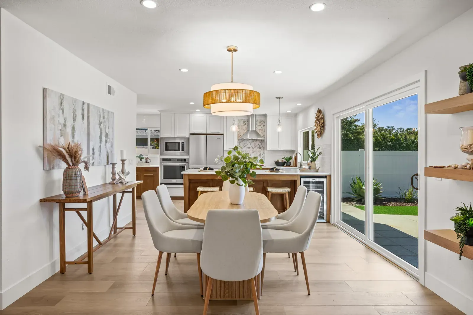 Bright modern dining room with round table, six chairs, pendant light, and sliding glass doors to a patio.