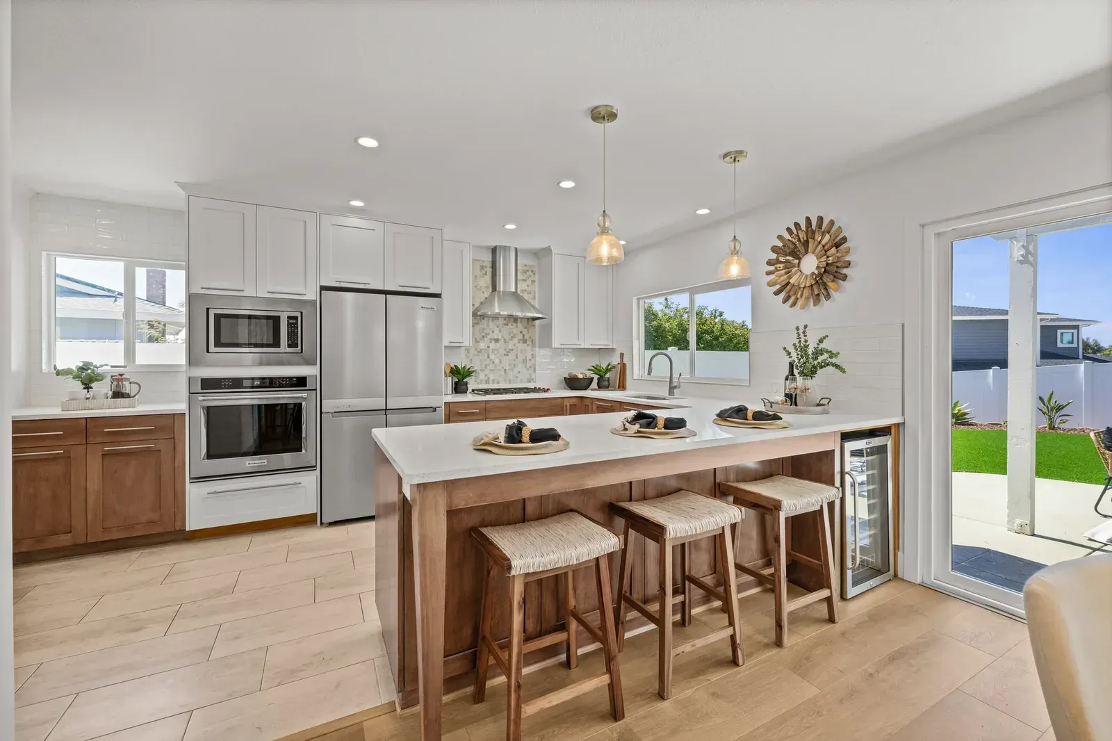 Bright modern kitchen with white cabinets, wood island, stools, and sliding glass doors to a patio