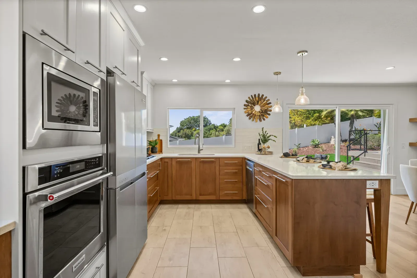 Modern kitchen with stainless appliances, wood cabinets, island, and large windows overlooking greenery