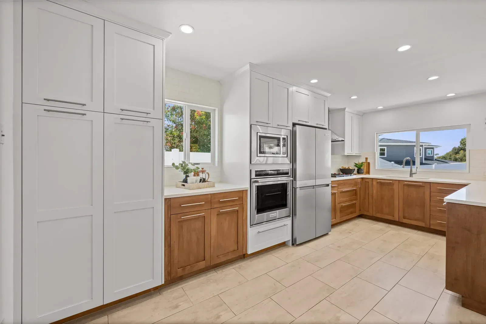 Bright modern kitchen with white cabinets, wood lower cabinets, stainless appliances, and tile floor