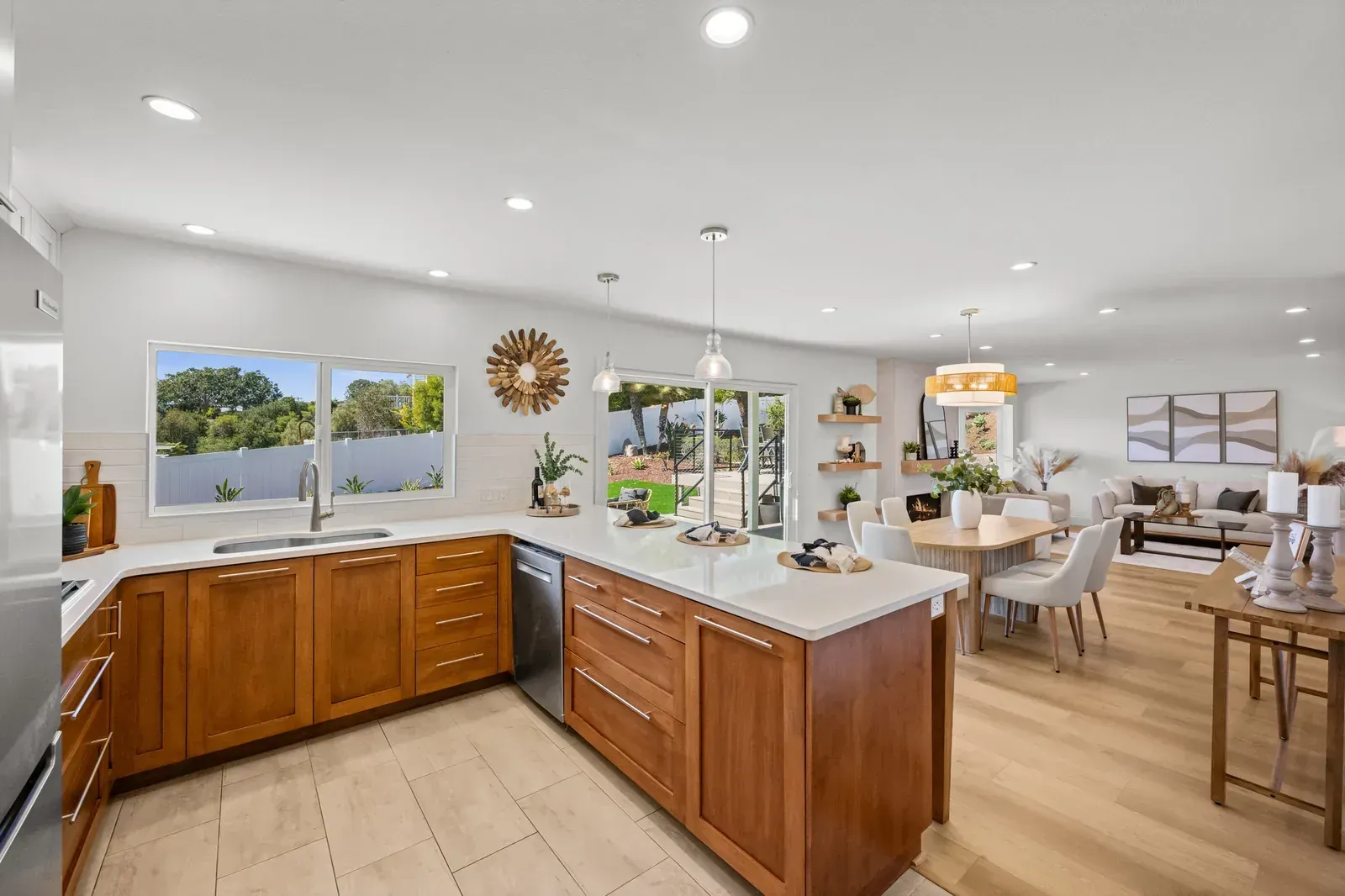 Bright open kitchen and dining area with wood cabinets, white walls, island, and large windows.