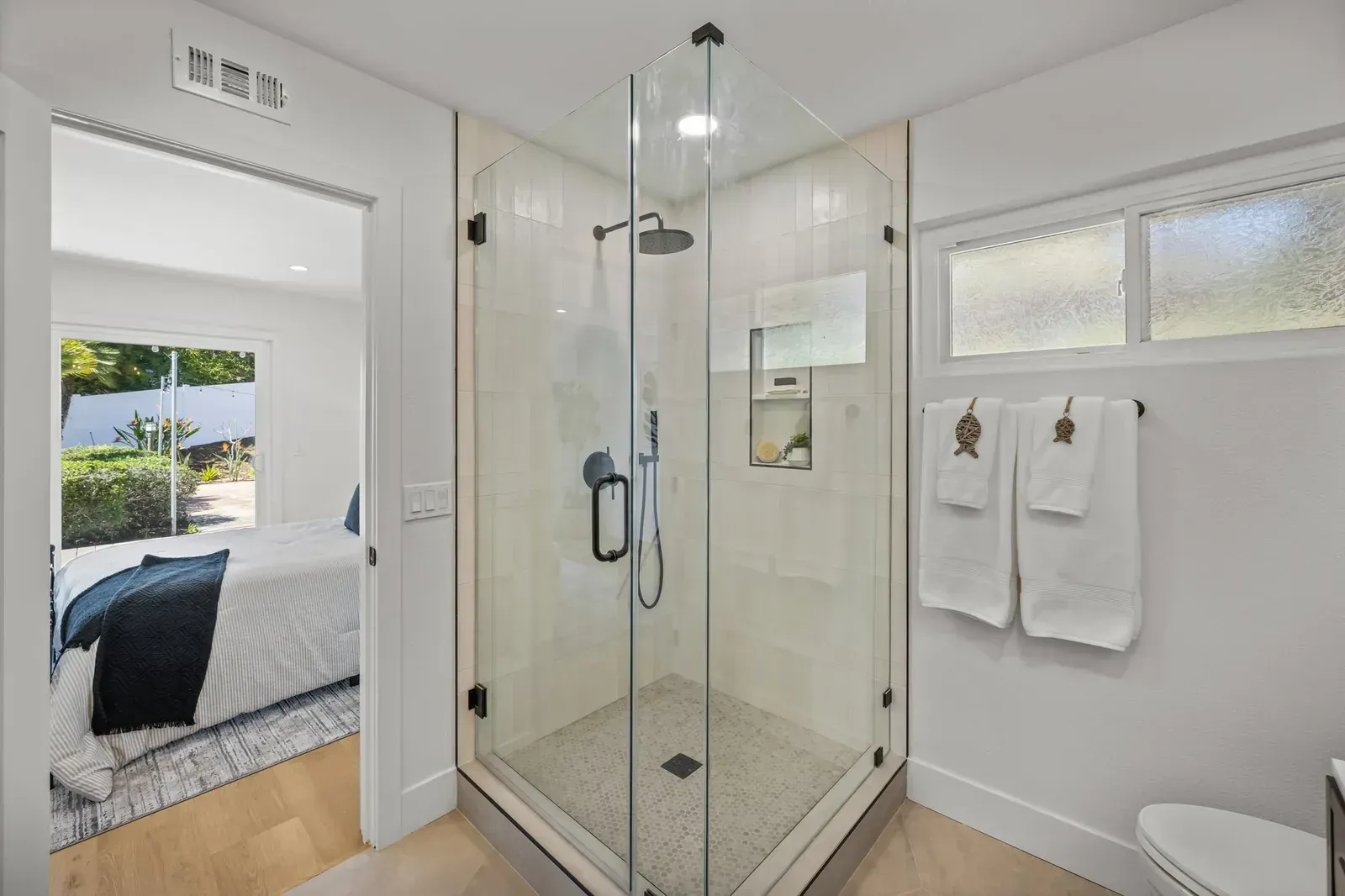 Bright modern bathroom with glass shower, white walls, and towels by a window.