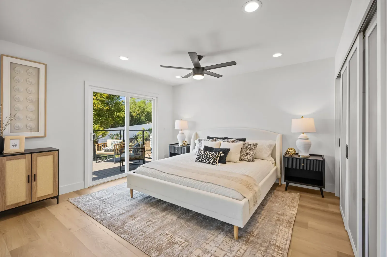 Bright modern bedroom with a white bed, ceiling fan, lamps, and sliding doors to a patio