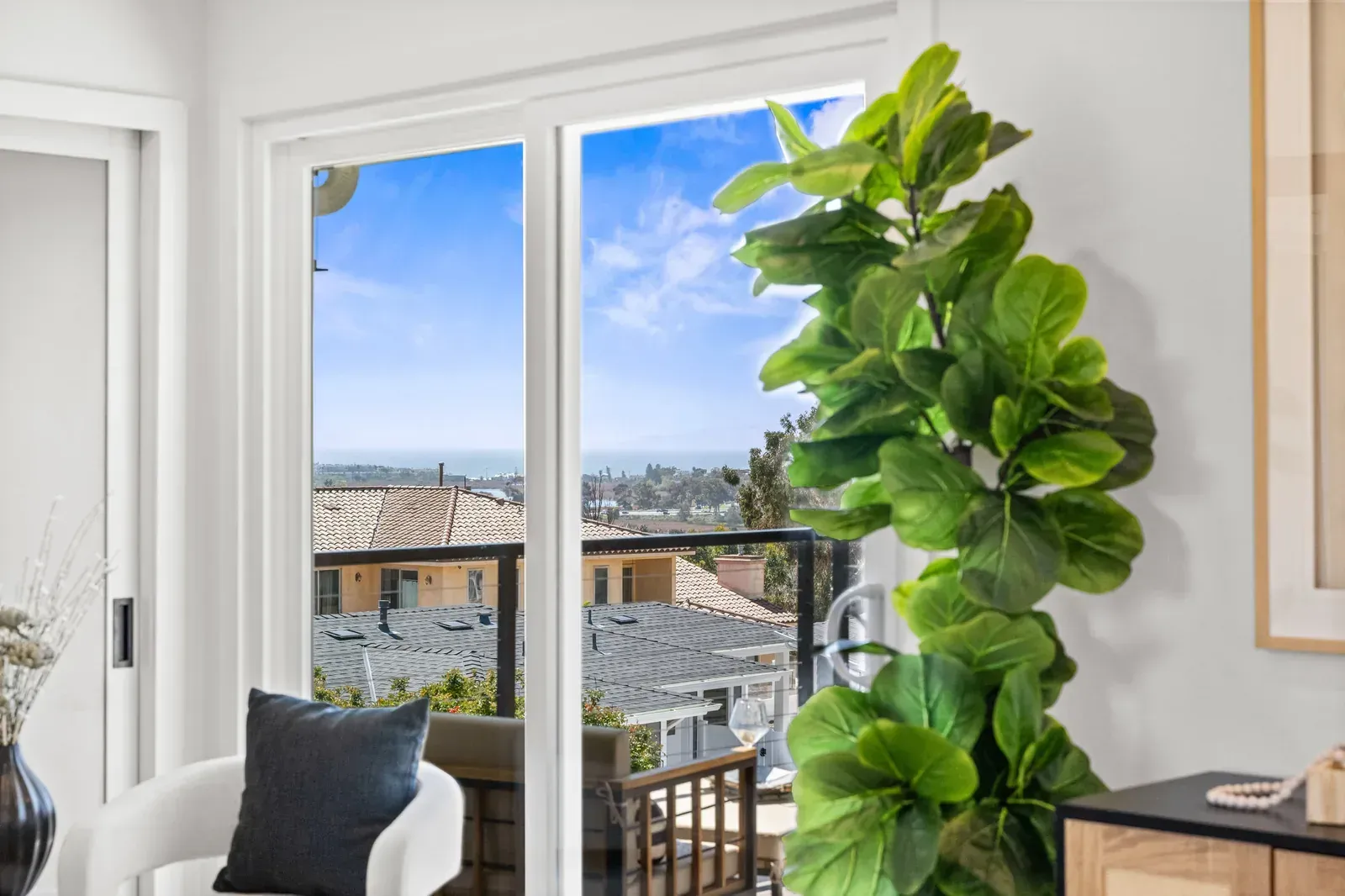 Bright living room with open balcony doors, city view, and a tall leafy plant by the window.