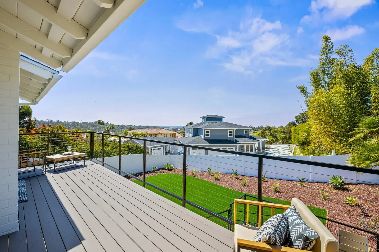 Backyard deck overlooking a waterfront home, green lawn, and bright blue sky