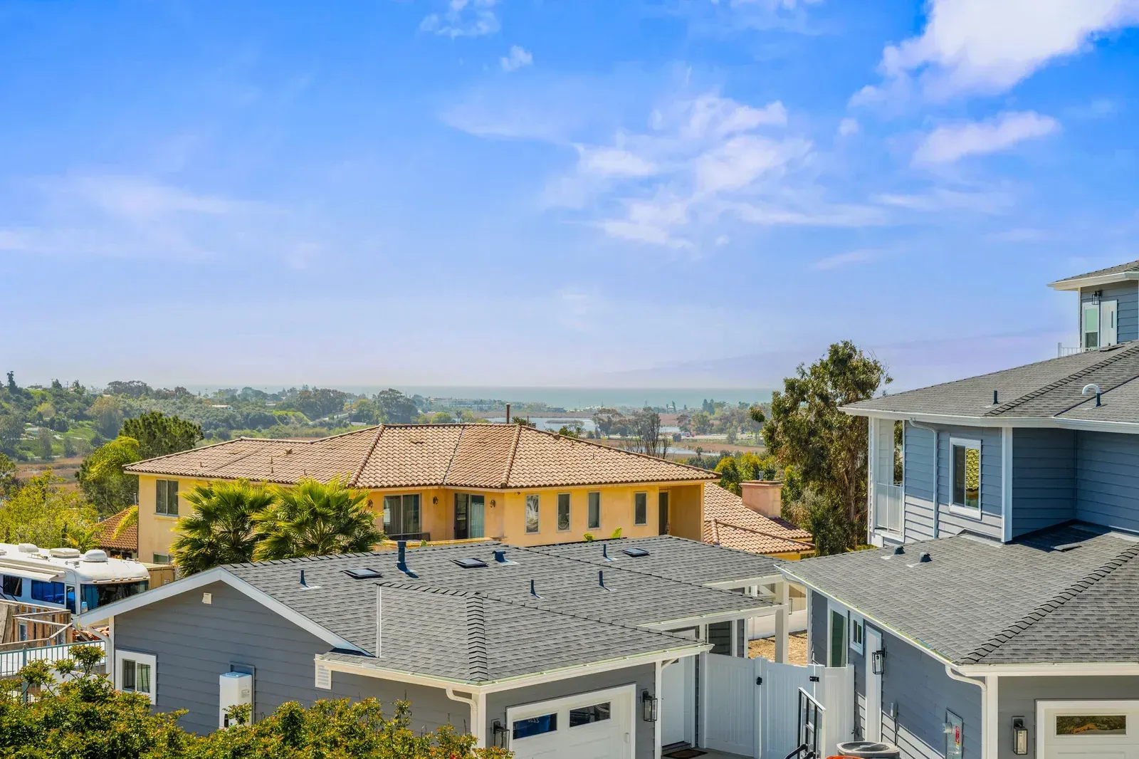 Suburban hillside homes with gray roofs under a blue sky, overlooking a distant valley
