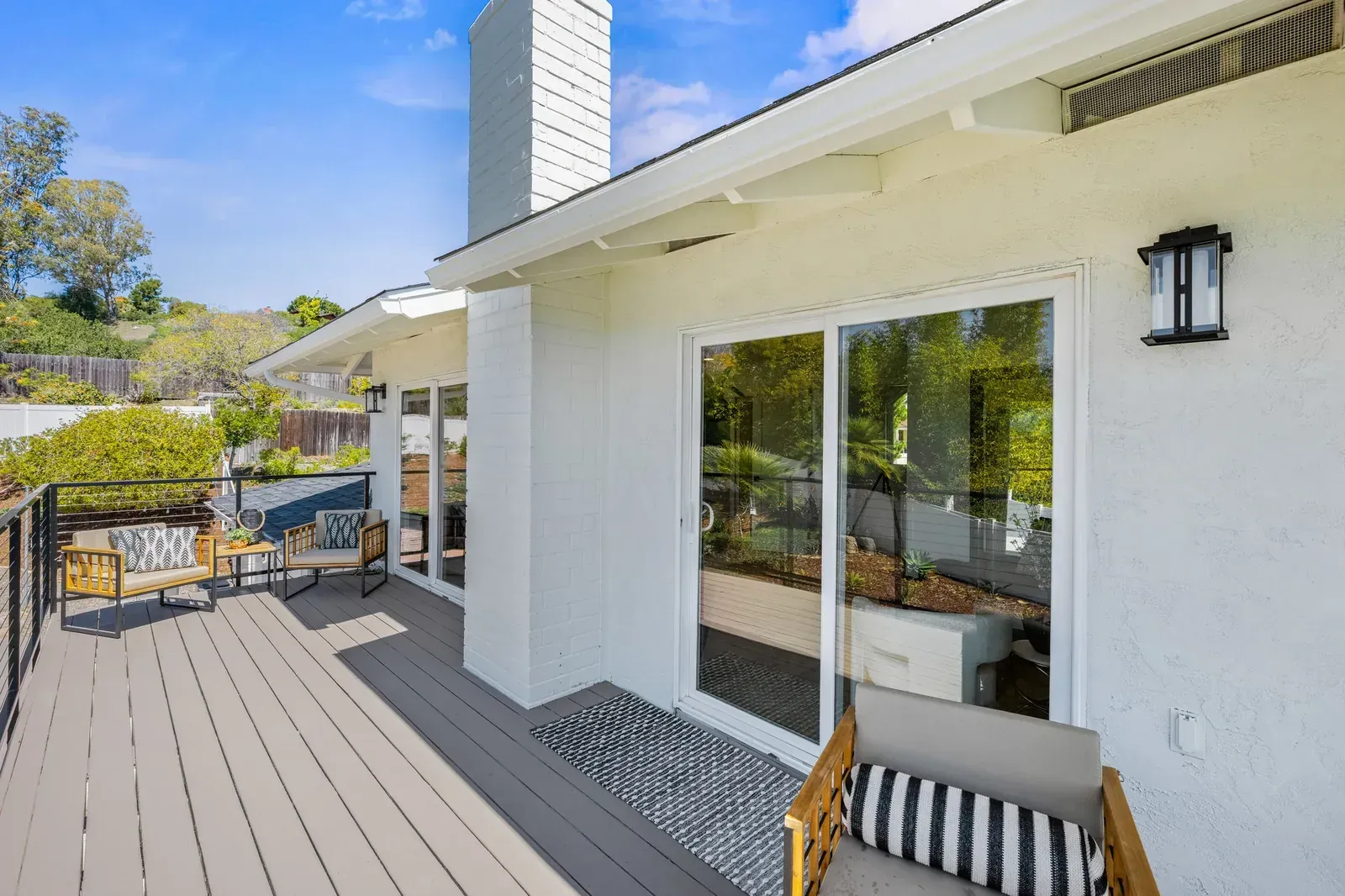 Sunny patio with white house exterior, sliding glass door, deck seating, and hillside garden view