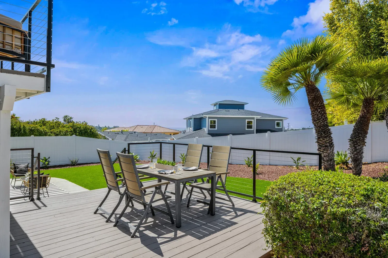 Patio with table and chairs overlooking a white-walled yard under a bright blue sky