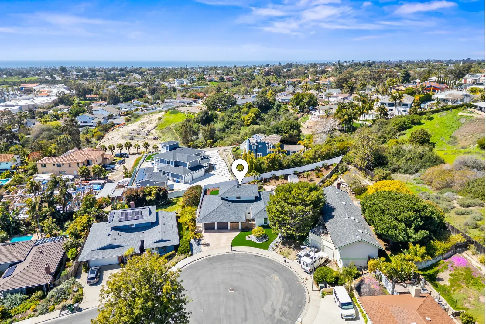 Aerial view of a suburban neighborhood with houses, streets, trees, and a clear blue sky.