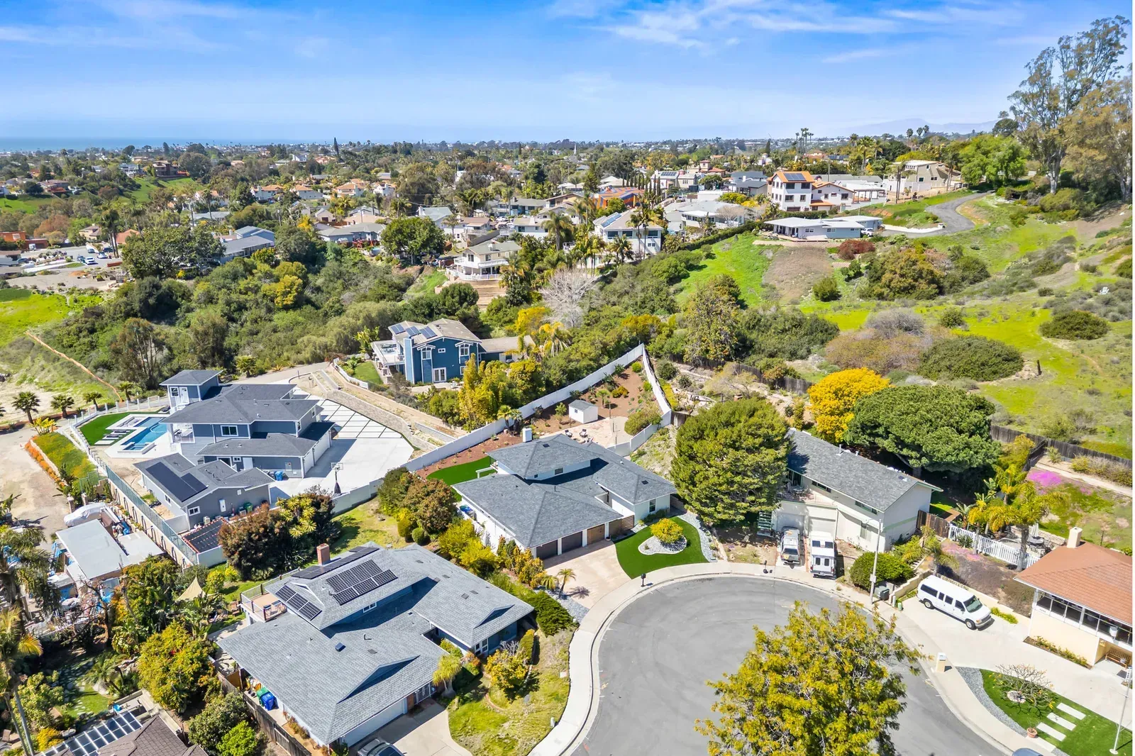 Aerial view of a suburban neighborhood with homes, winding streets, and green hills under a clear sky