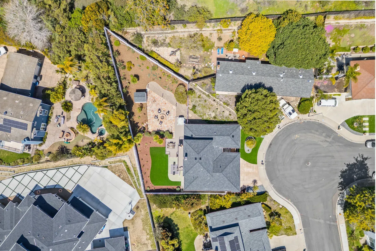Aerial view of a suburban house with a gray roof, landscaped yard, and a cul-de-sac street nearby.