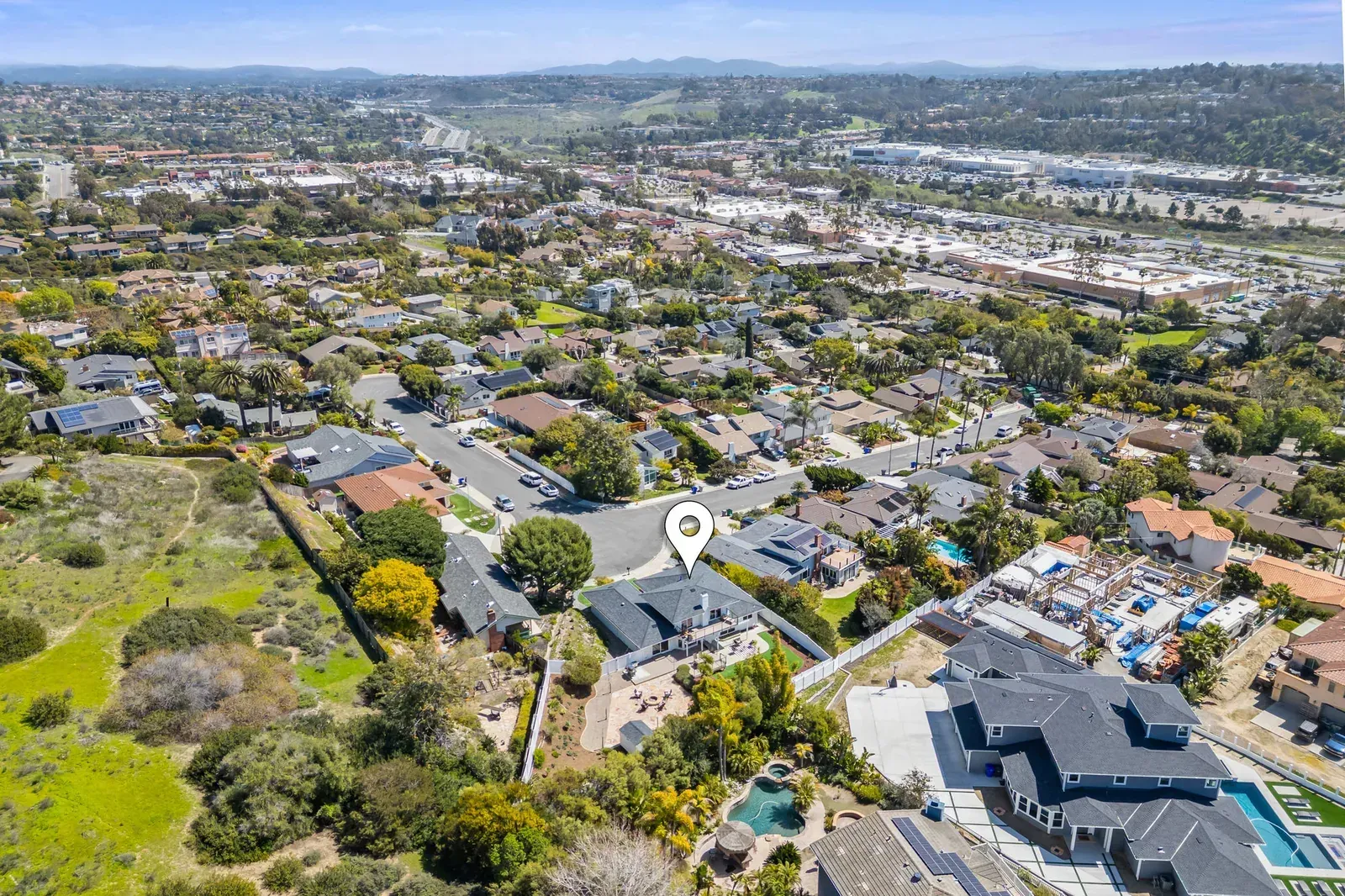 Aerial view of a suburban neighborhood with houses, streets, and hills in the distance.