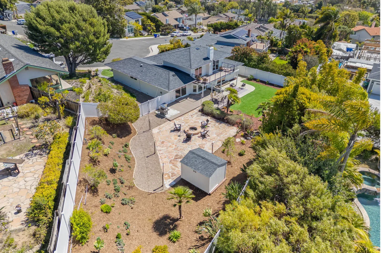 Aerial view of a house with a backyard patio, garden beds, and surrounding trees.