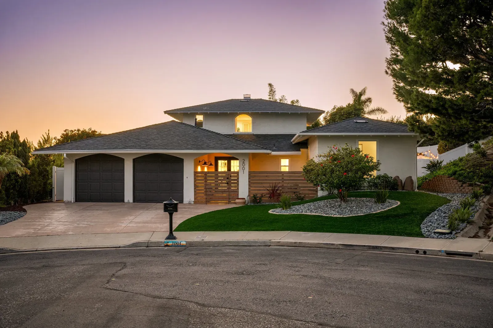 Suburban house at dusk with lit windows, two-car garage, and a manicured front lawn