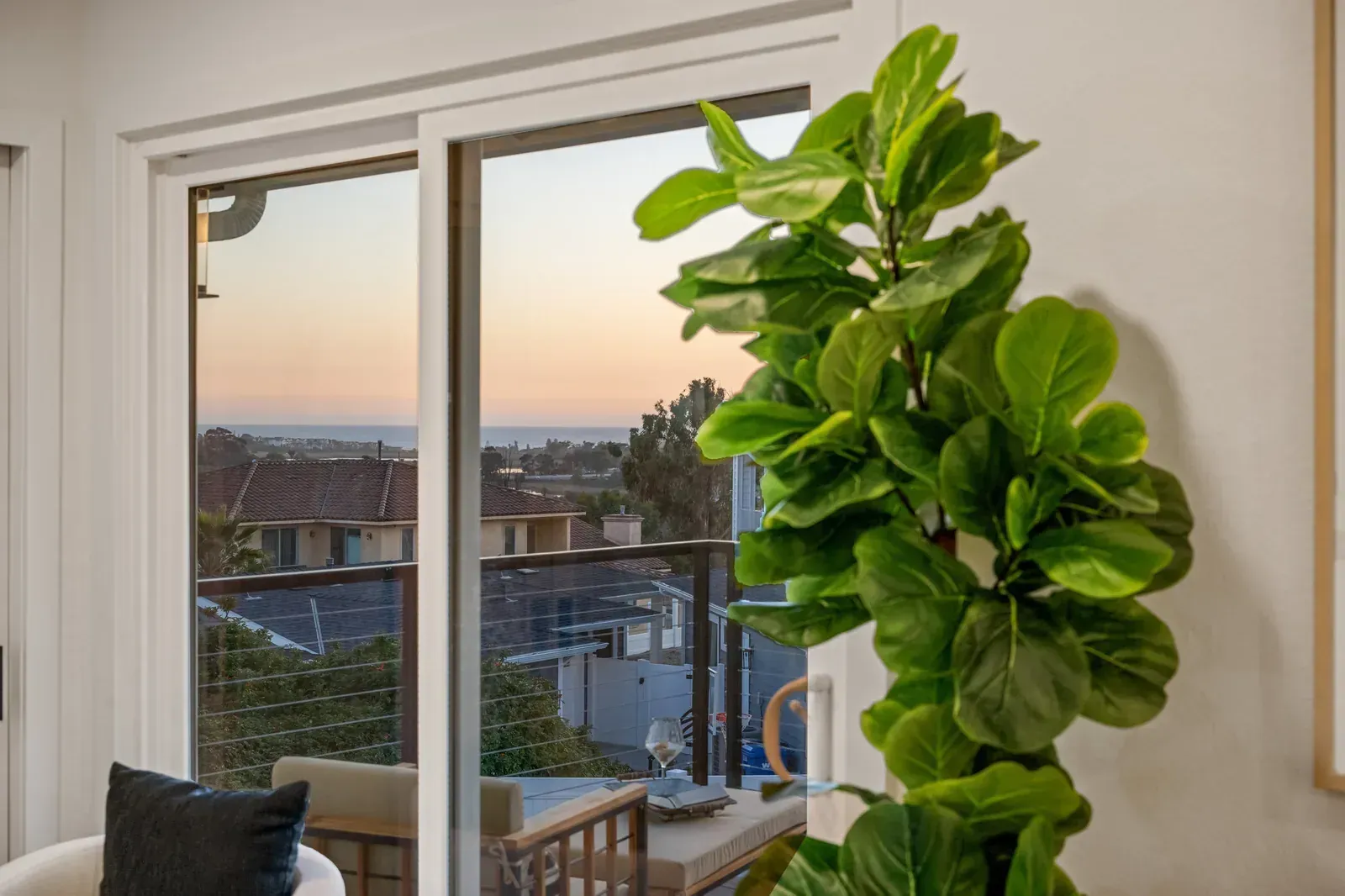 Living room with a balcony view at sunset and a tall green plant by the window