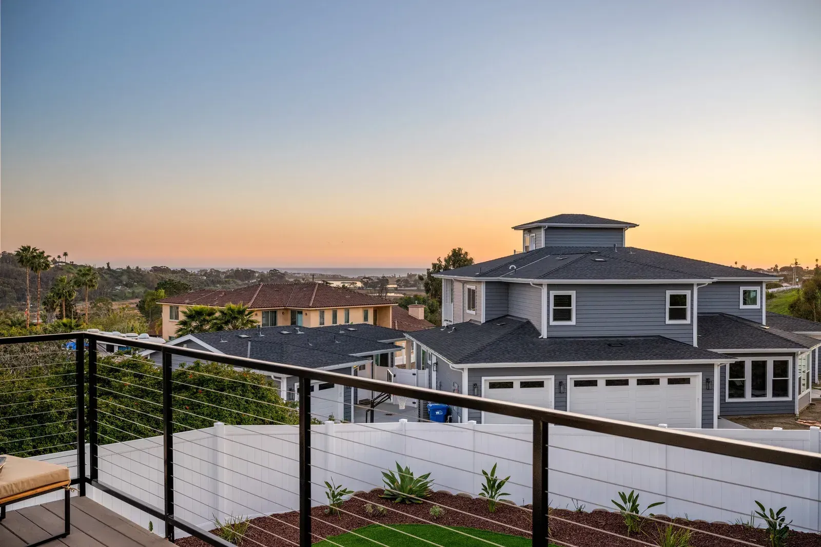 Rooftop terrace with black railing and city homes at sunset over a distant landscape