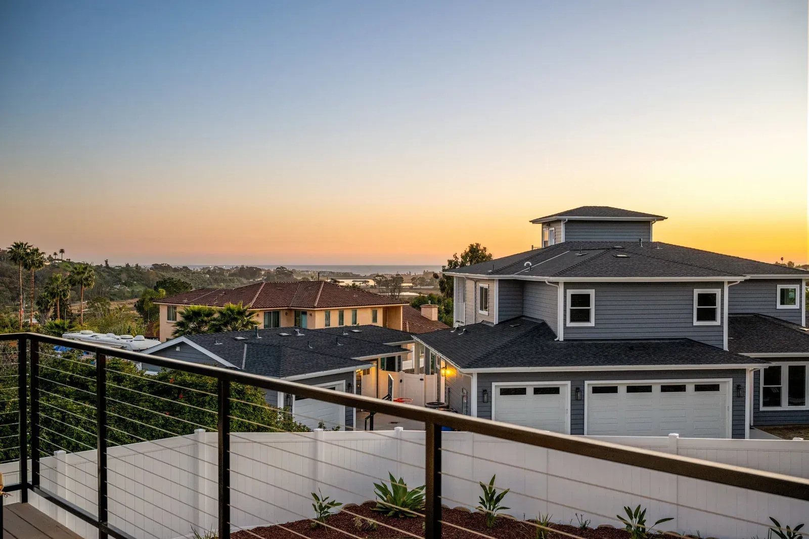 Sunset view over suburban homes and a pool, seen from a balcony with black railing.