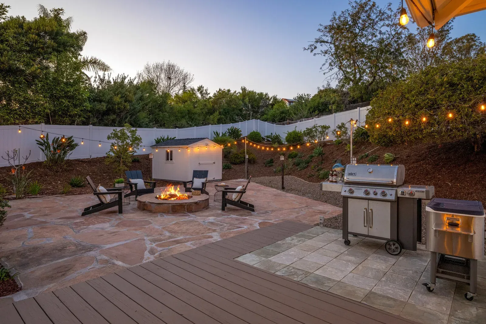 Backyard patio with fire pit, string lights, outdoor seating, and grill at dusk