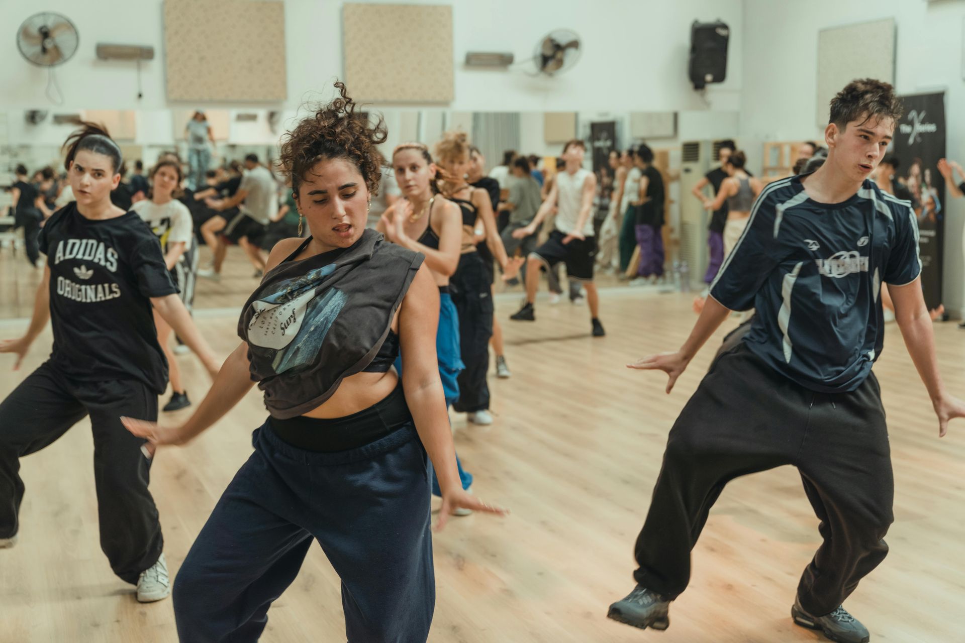 Een dansles in een studio. Mensen van diverse leeftijden en etniciteiten dansen energiek. Spiegels op de achtergrond.