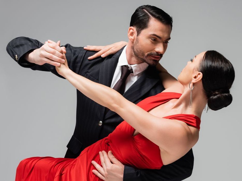 Man in pak danst tango met vrouw in rode jurk.