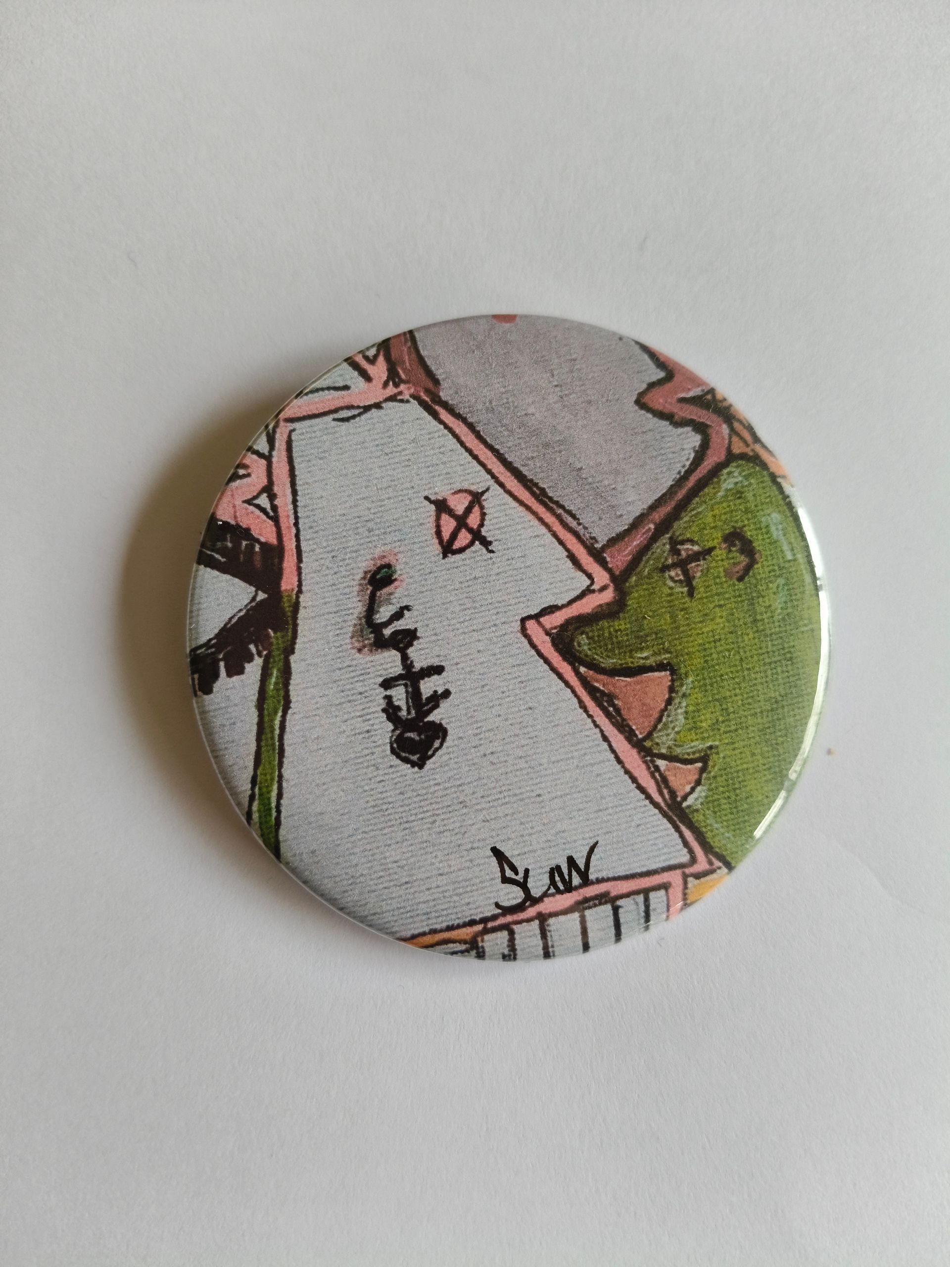 Een ronde speld met een handgetekend, abstract ontwerp met roze, groene en grijze vormen en kleine zwarte symbolen.