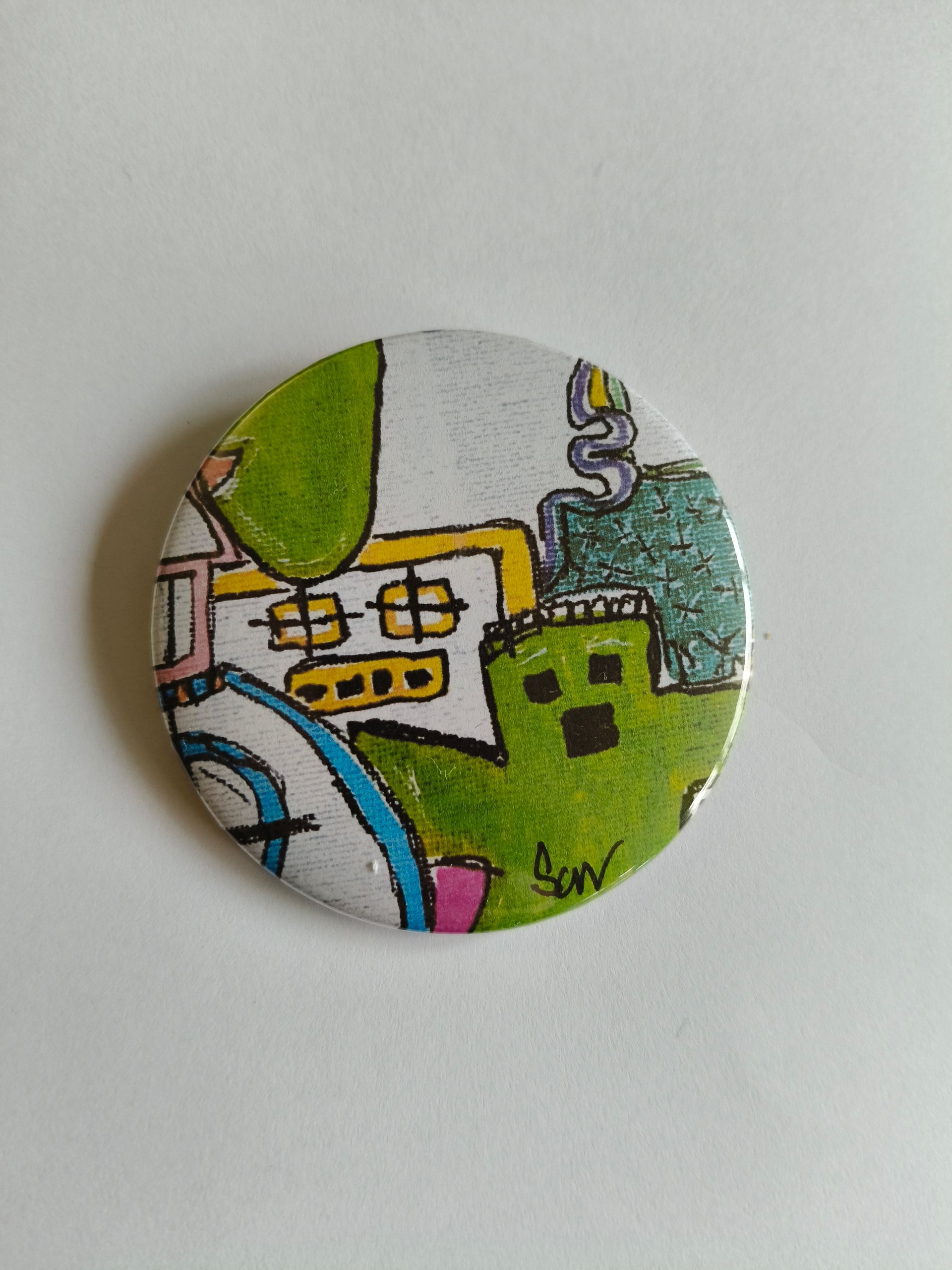 Een ronde button game met een speelse, handgetekende illustratie van een groen spook, een geel huis en blauwe accenten.