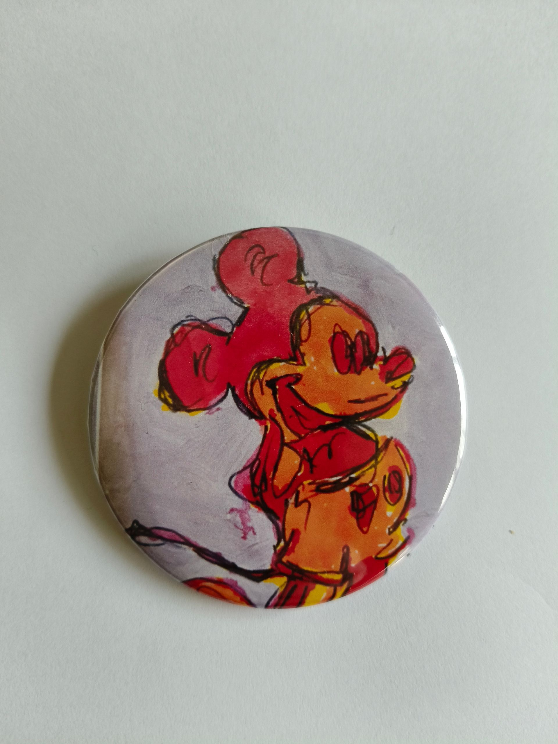 Een ronde speld met een expressieve, abstracte tekening van Mickey Mouse uitgevoerd in oranje en roze tinten.