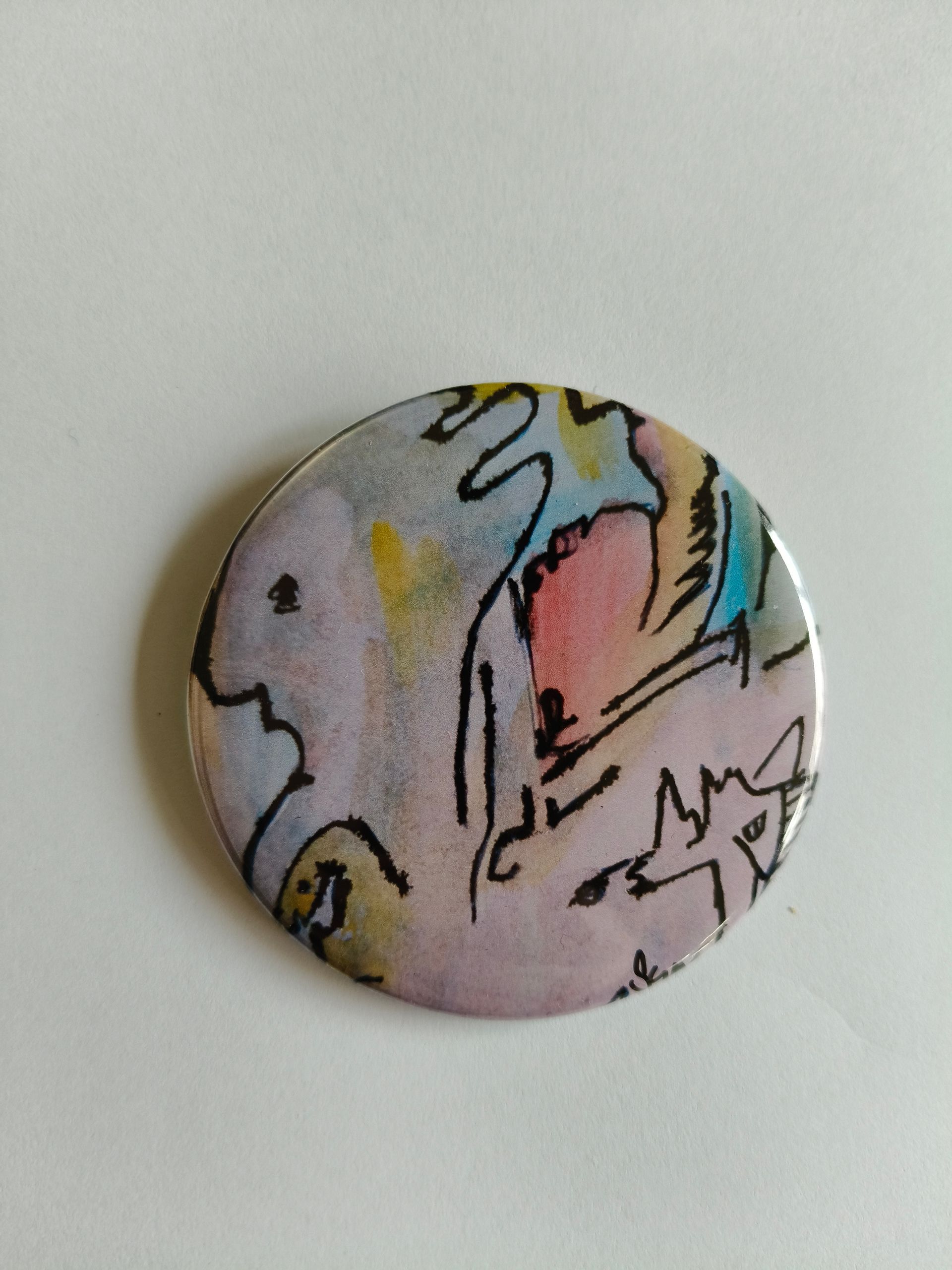 Een ronde speld met abstracte illustraties in inkt en aquarel van meerdere gestileerde figuren tegen pastelkleuren.