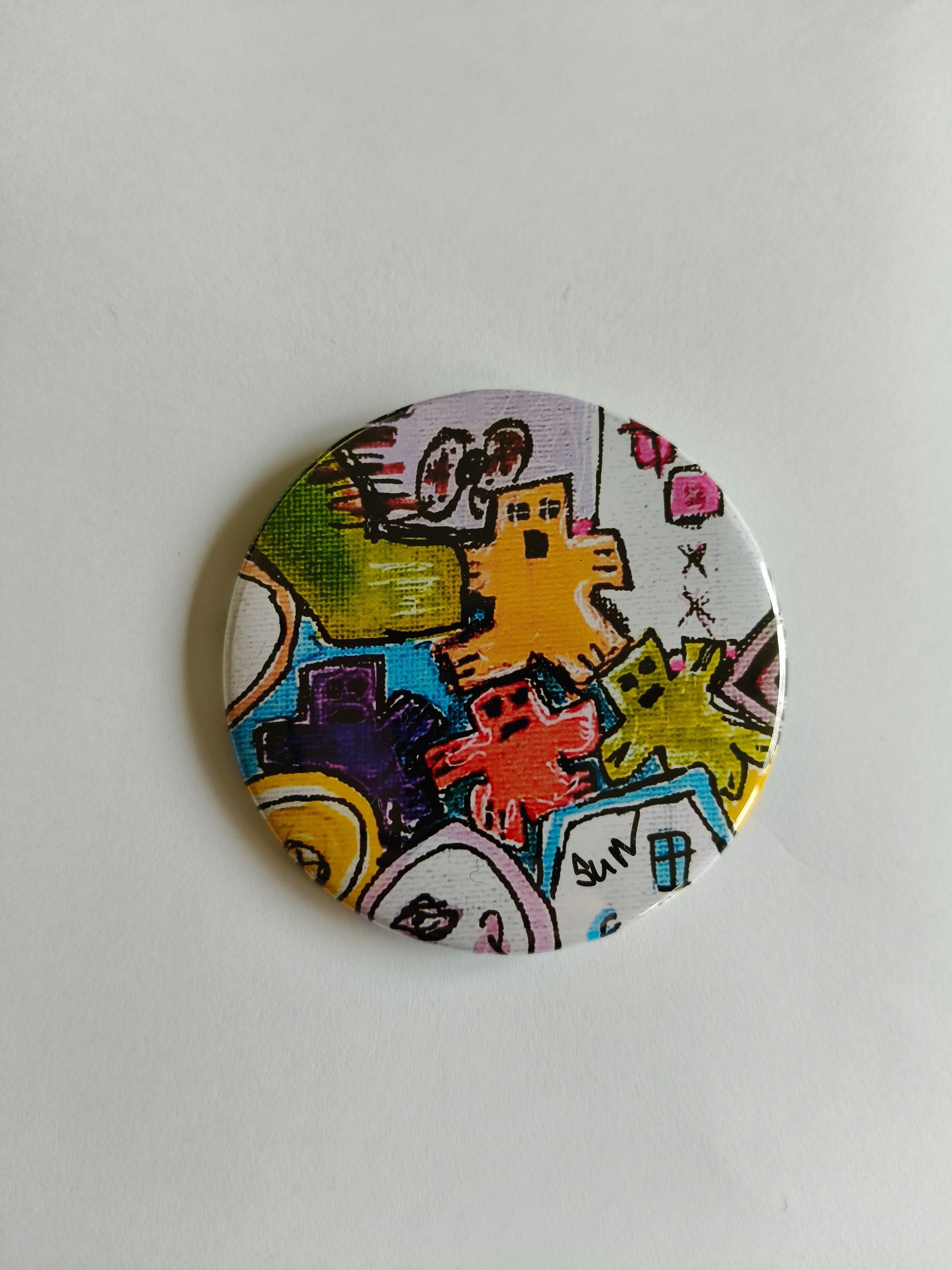 Een ronde button met een kleurrijke, handgetekende afbeelding van verschillende gestileerde wezens en vormen.