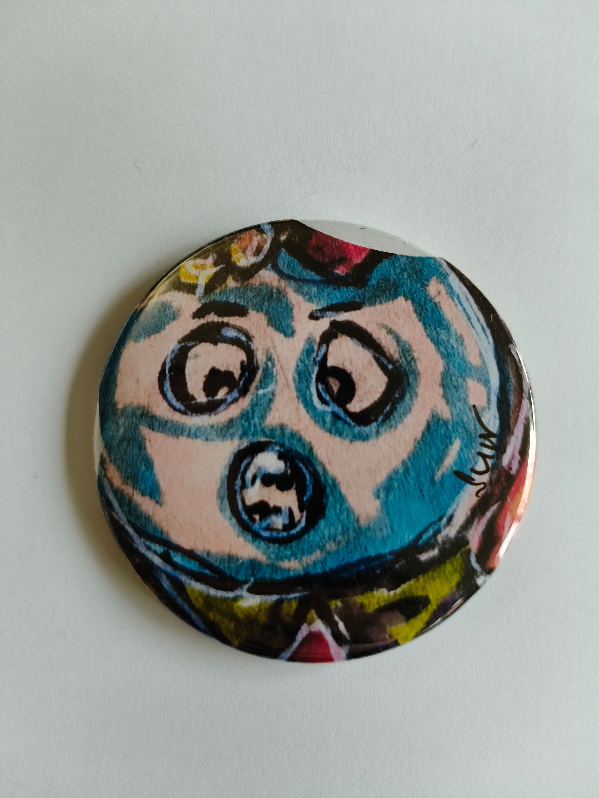 Een ronde button met een handgetekende illustratie van een blauw, verbaasd kijkend wezentje met grote ogen.