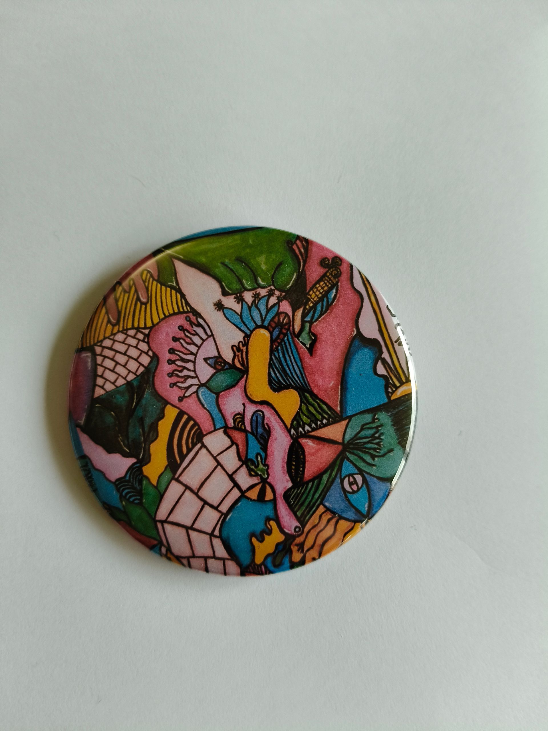 Een ronde speld met een levendige, abstracte tekening met kleurrijke vormen, ingewikkelde patronen en dikke zwarte contouren.