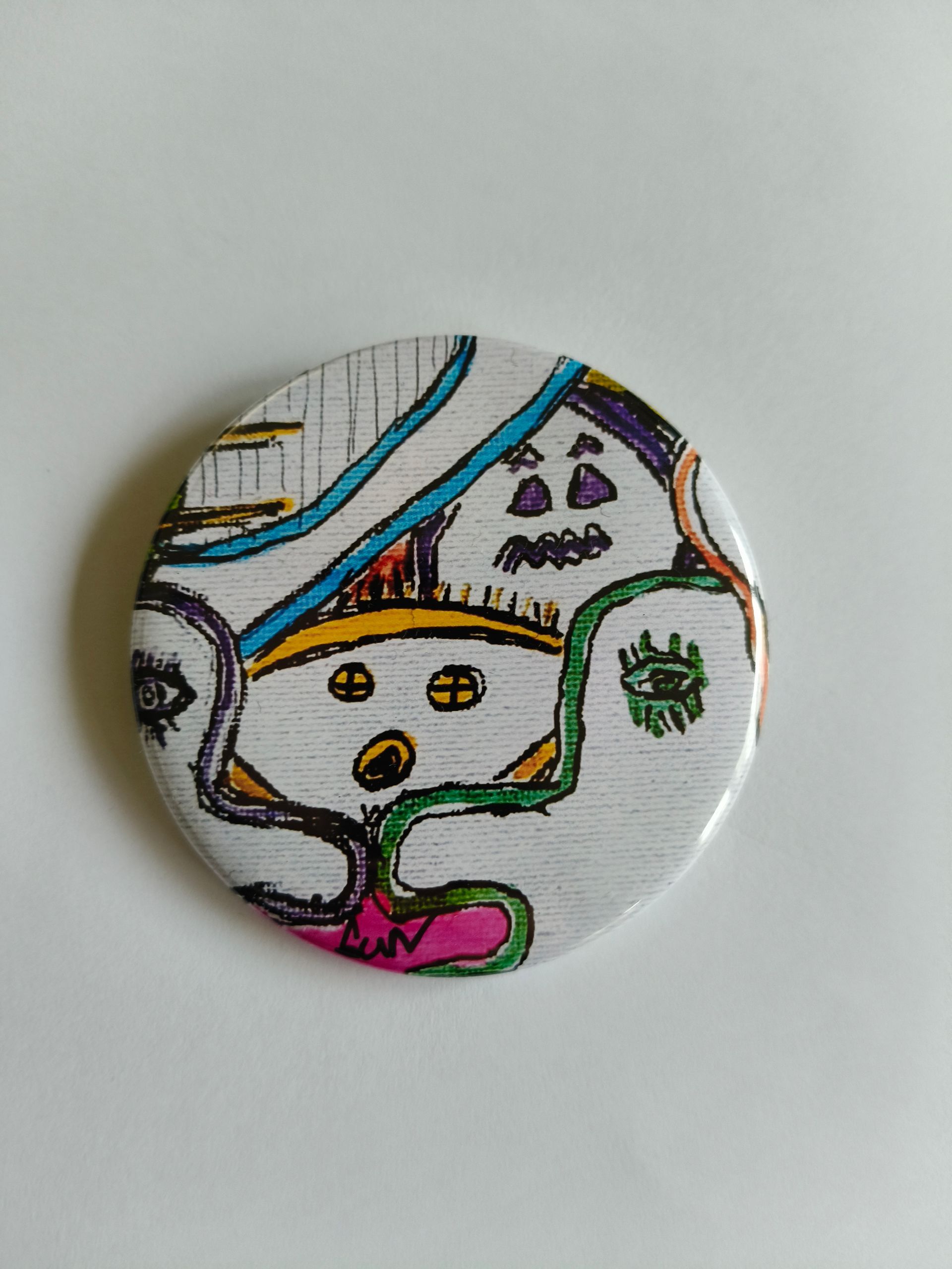 Een ronde speld met een kleurrijke, handgetekende doodle met ogen, een geschrokken gezicht en kronkelende abstracte lijnen.