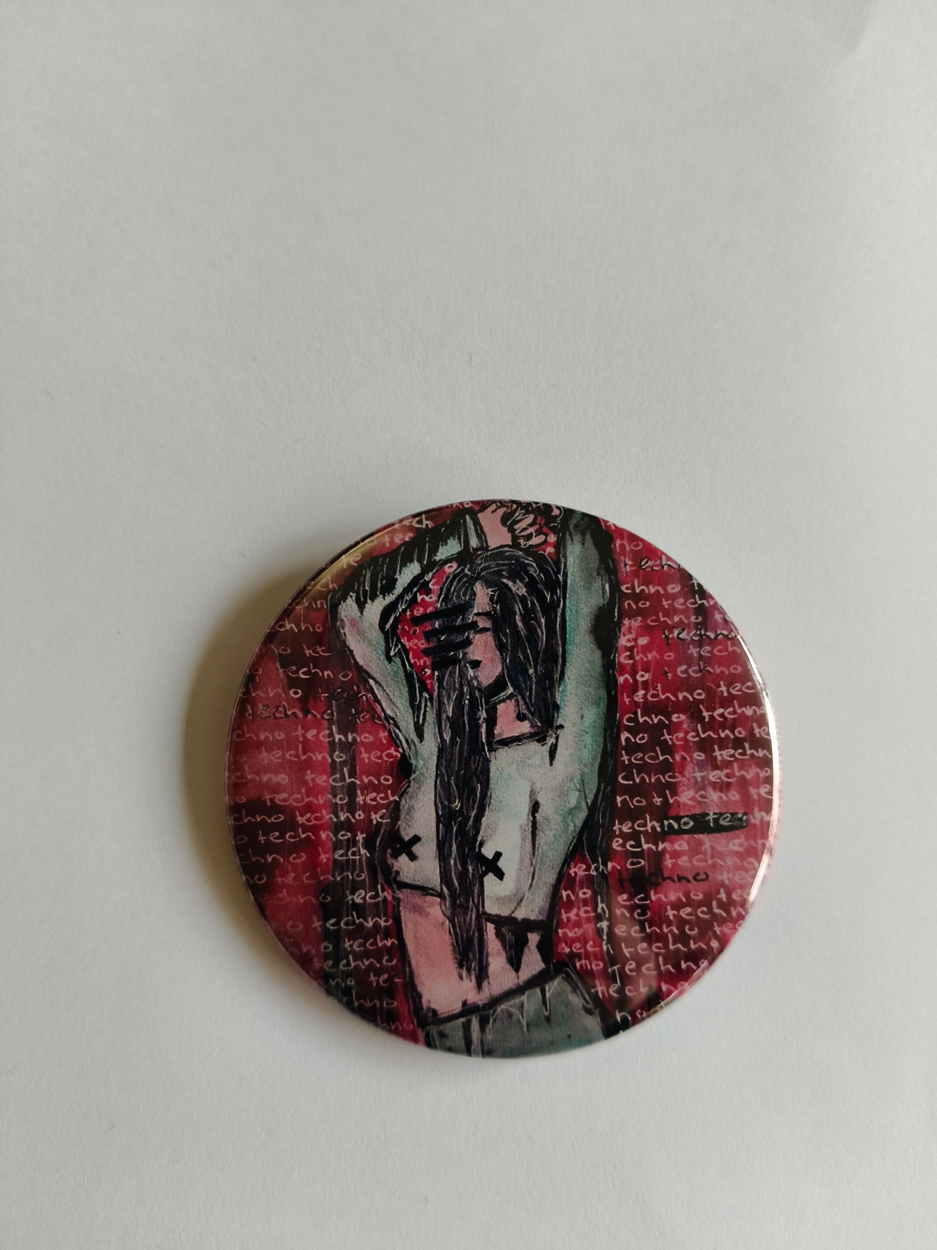 Een ronde button met een gestileerde afbeelding  persoon met lang haar en opgeheven armen tegen een rode.