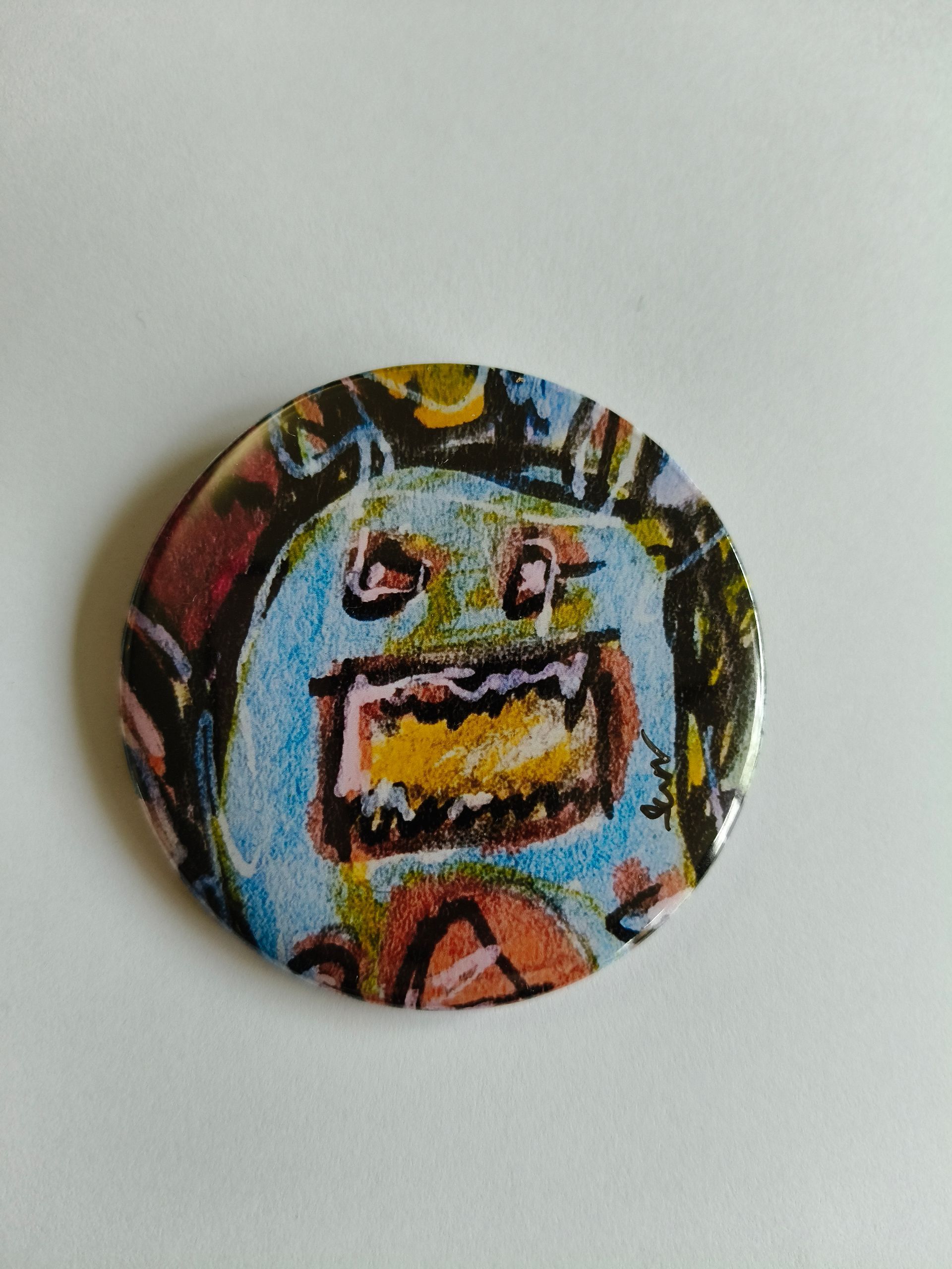 Een rond buttonbadge met een kleurrijke, handgetekende illustratie van een monster met een brede, tandige bek.