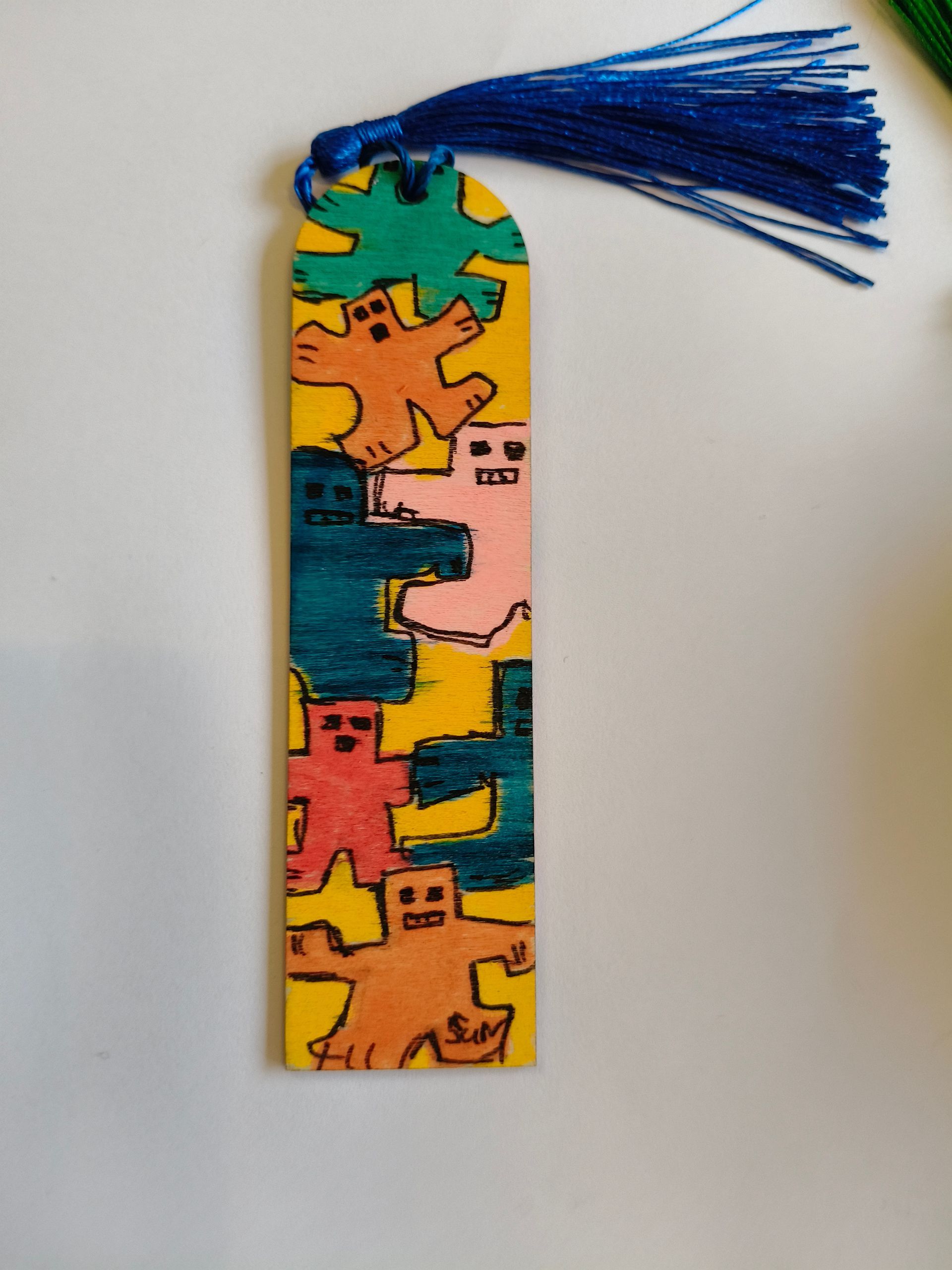Een gele boekenlegger met kleurrijke, handgetekende figuurtjes in peperkoekstijl en een blauwe kwast bovenaan.